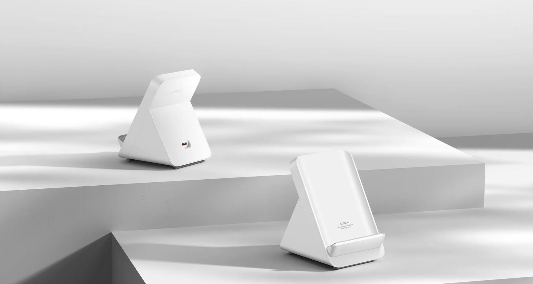 Dwie białe ładowarki bezprzewodowe na białej platformie. Jedna pod kątem, druga pionowo. Obie mają logo Xiaomi.