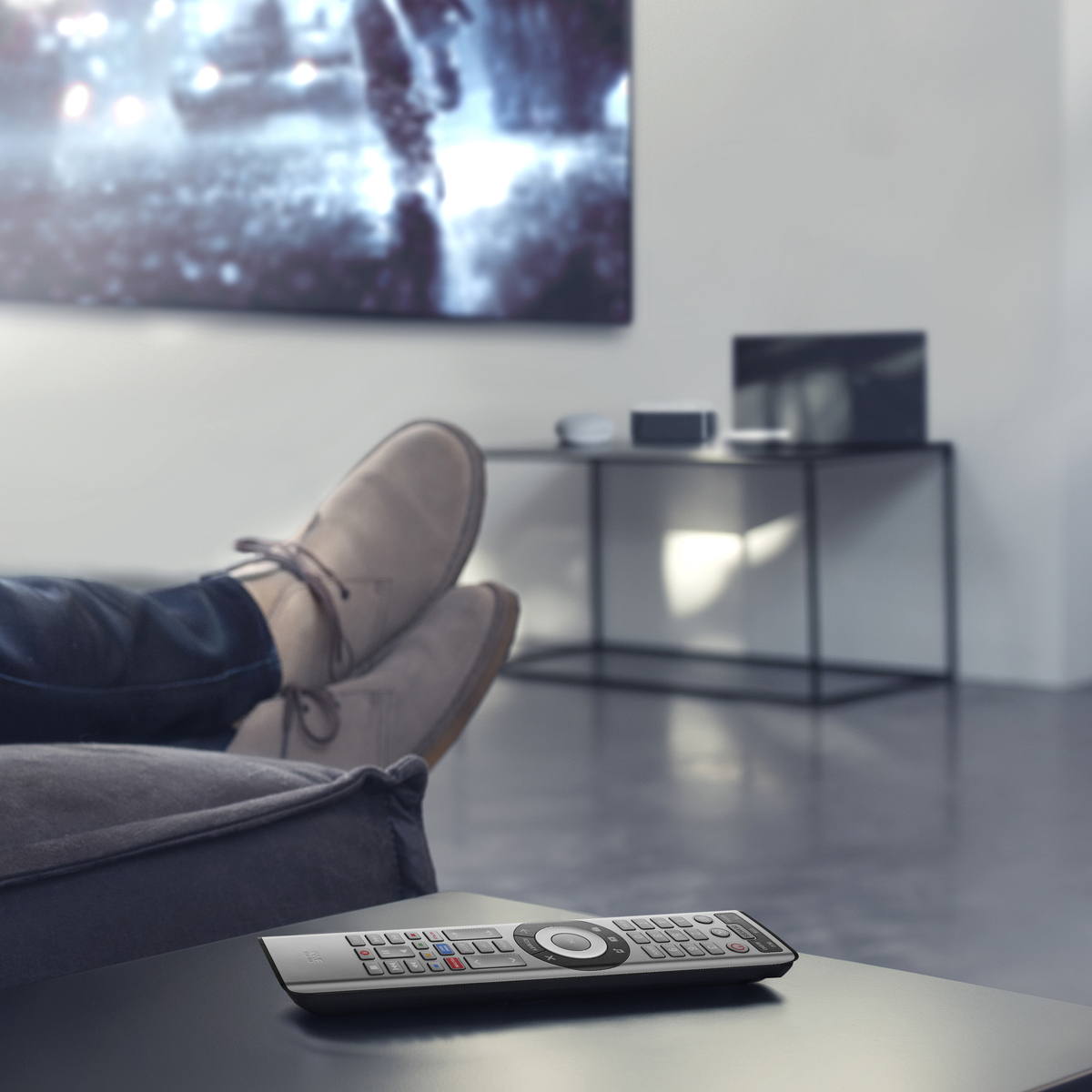 Eine Person liegt auf einem Sofa und hat eine Fernbedienung auf einem Tisch.