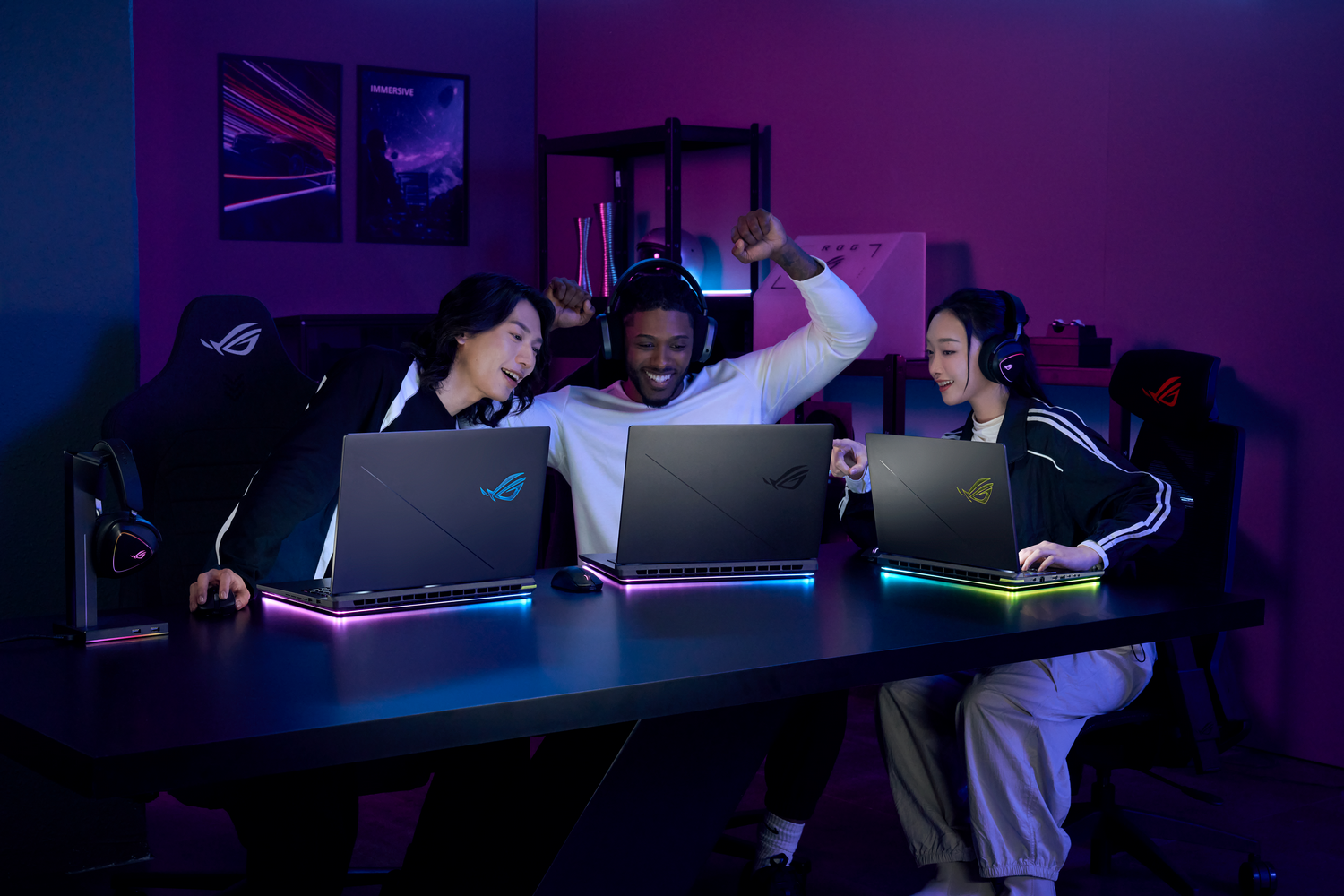 Tres personas jugando en portátiles gaming, con luces RGB y logos ROG en una mesa oscura.