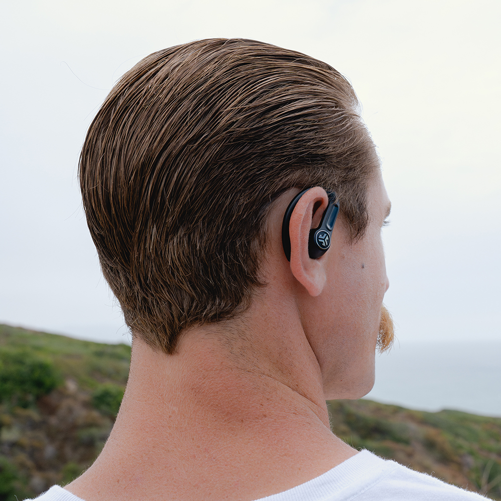 Mężczyzna ze słuchawkami w jednym uchu, patrzący w bok. Na zewnątrz.