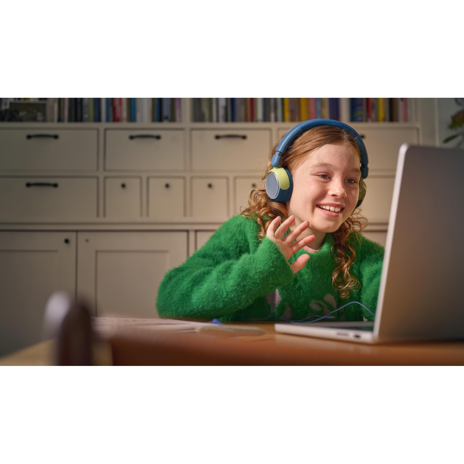Una ragazza con un maglione verde sorride e videochatta su un laptop.