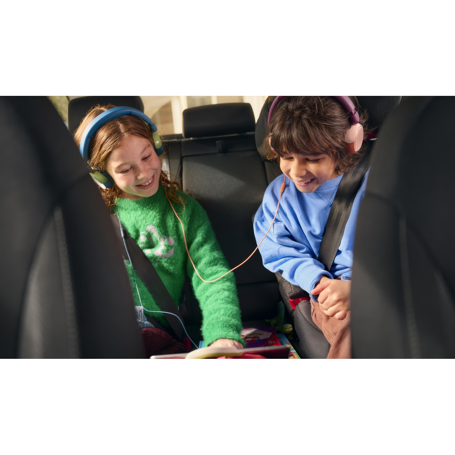 Due bambini in auto, con le cuffie e che guardano un tablet.