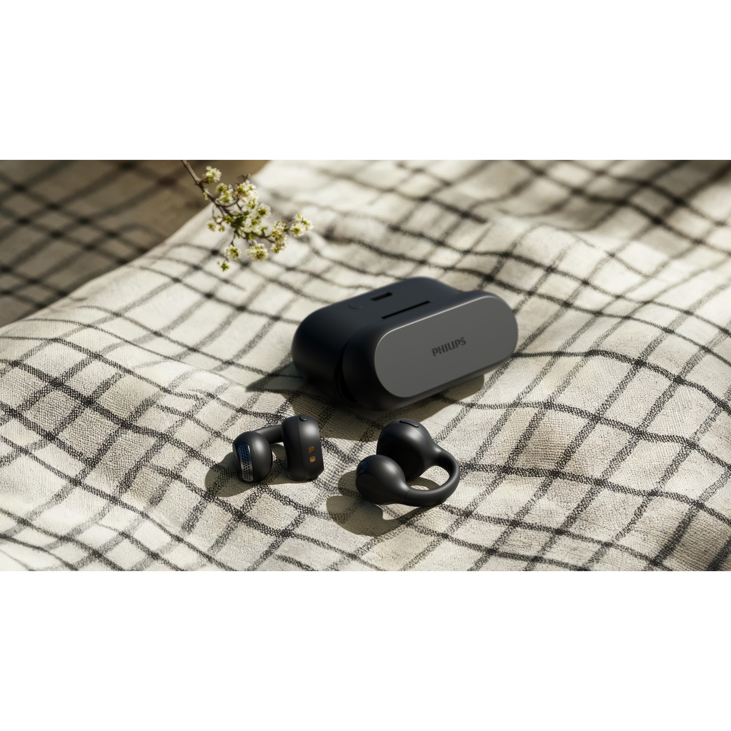 Auricolari neri e custodia di ricarica su coperta a scacchi con fiori.