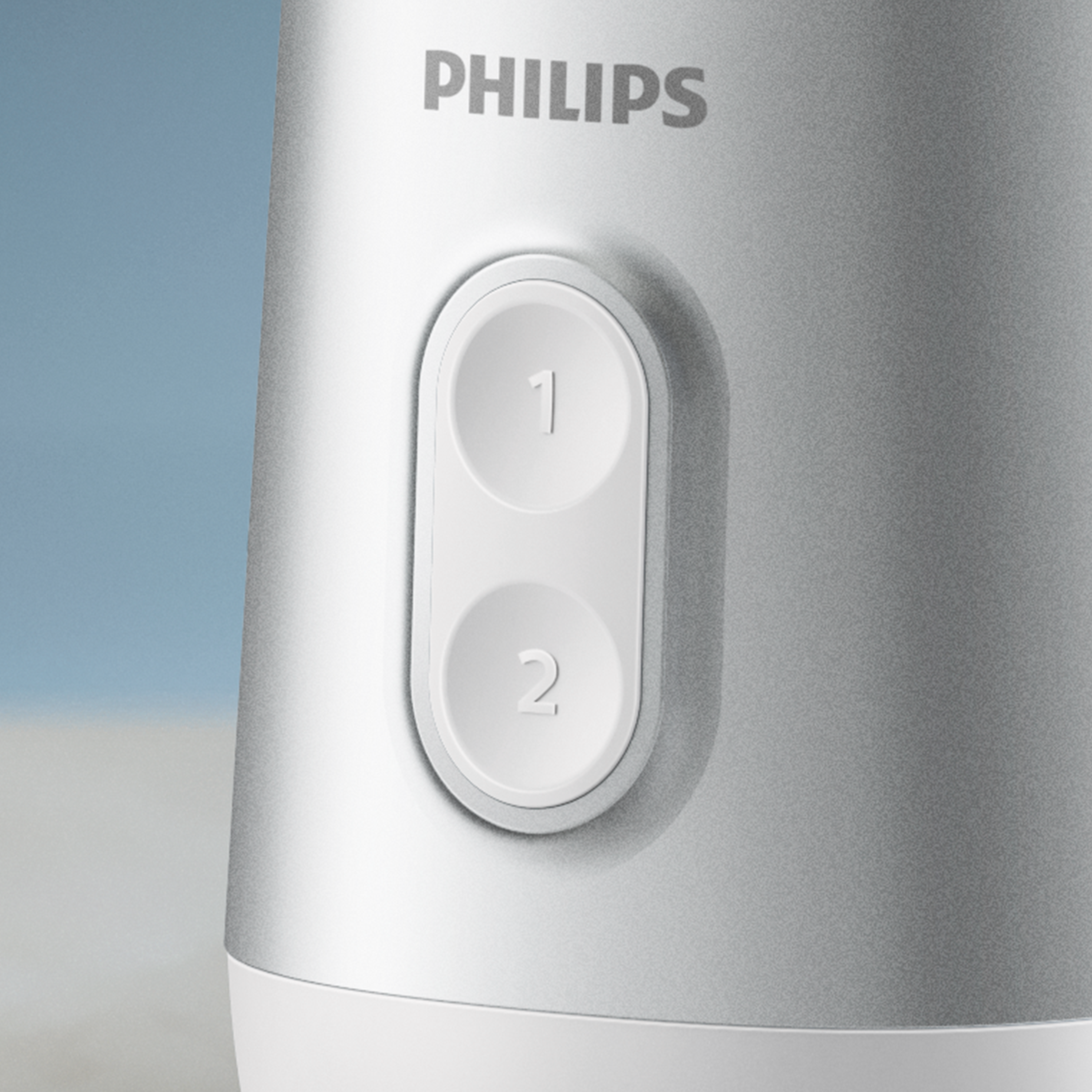 Egy ezüst turmixgép közelképe Philips márkajelzéssel, két fehér gombot mutatva, 1-es és 2-es felirattal.