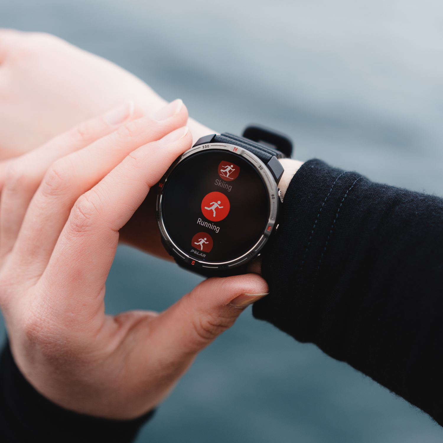 Persona usando un reloj inteligente, con opciones de esquí y carrera. El reloj muestra iconos en una pantalla negra.