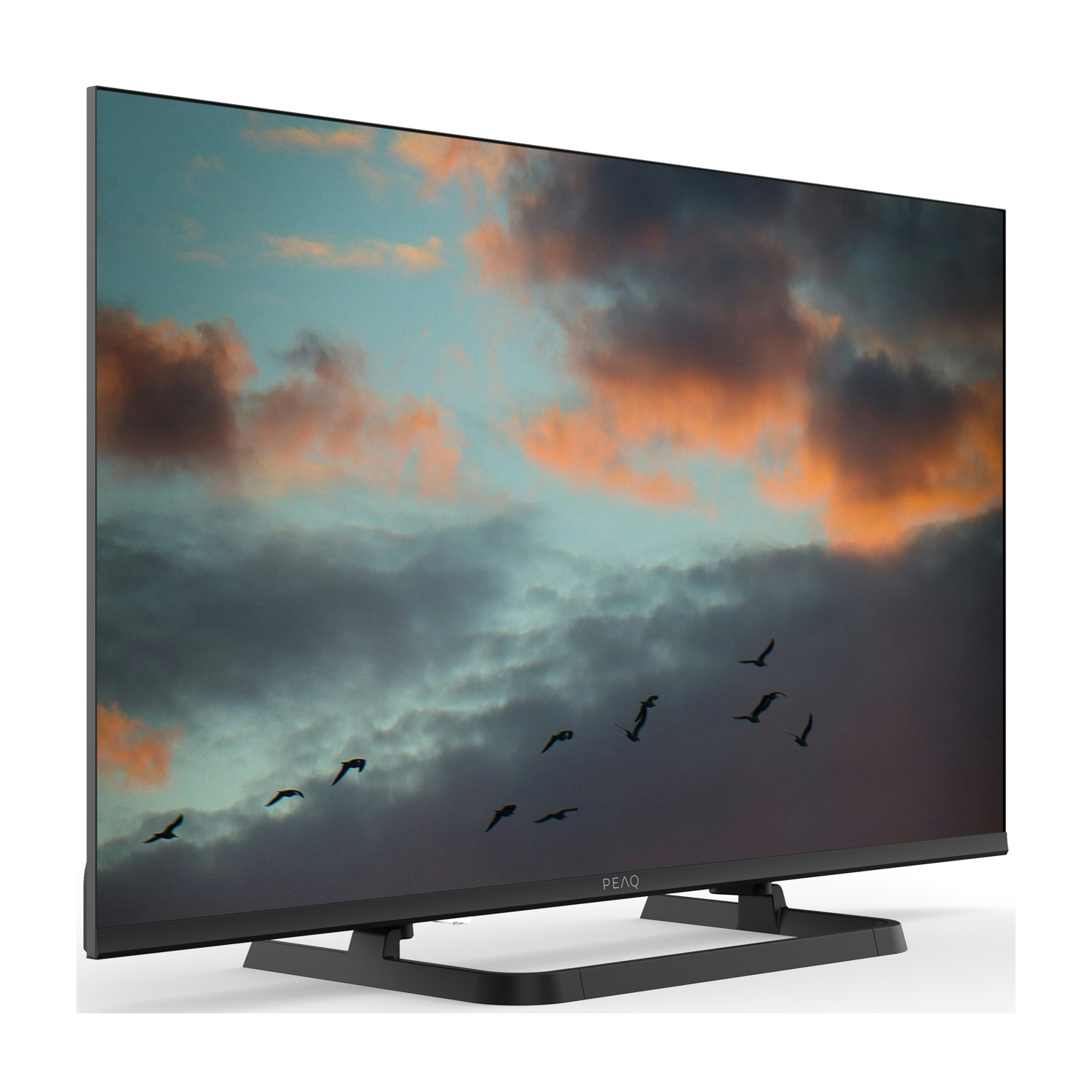 Una TV mostra un tramonto con uccelli in volo. La TV è nera e su una superficie bianca. Il cielo ha nuvole arancioni, blu e grigie.