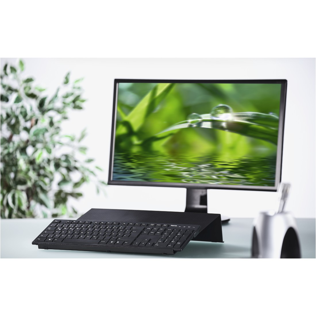 Schwarze Tastatur auf einem Ständer, Monitor zeigt Wassertropfen auf einem Blatt.