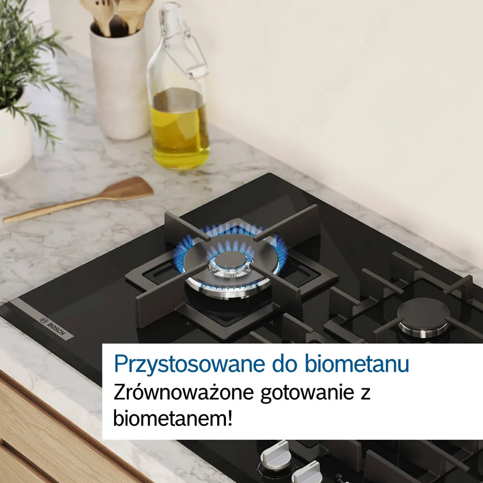 Kuchenka gazowa z zapalonym niebieskim płomieniem. Butelka oleju, drewniana łyżka i rośliny na blacie.