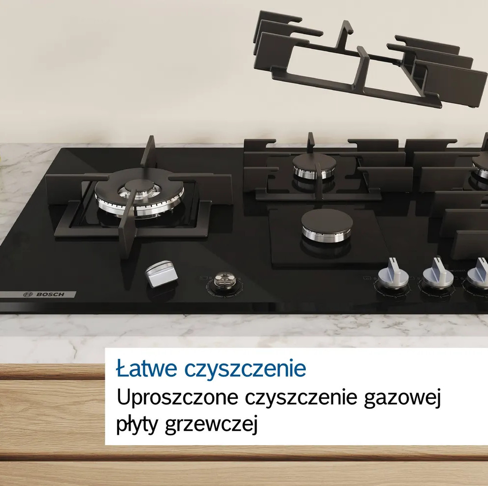 Czarna kuchenka gazowa z usuniętym rusztem. Biały blat i drewniane szafki poniżej.