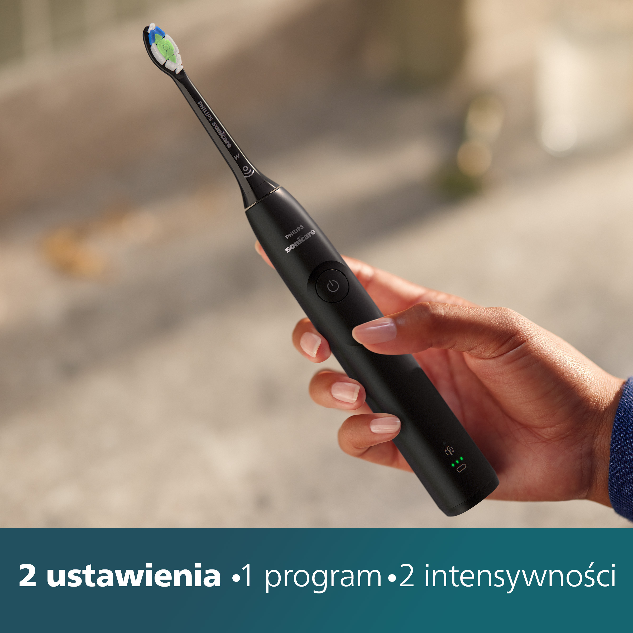 Dłoń trzymająca czarną szczoteczkę elektryczną. Tekst: 2 ustawienia, 1 program, 2 intensywności.