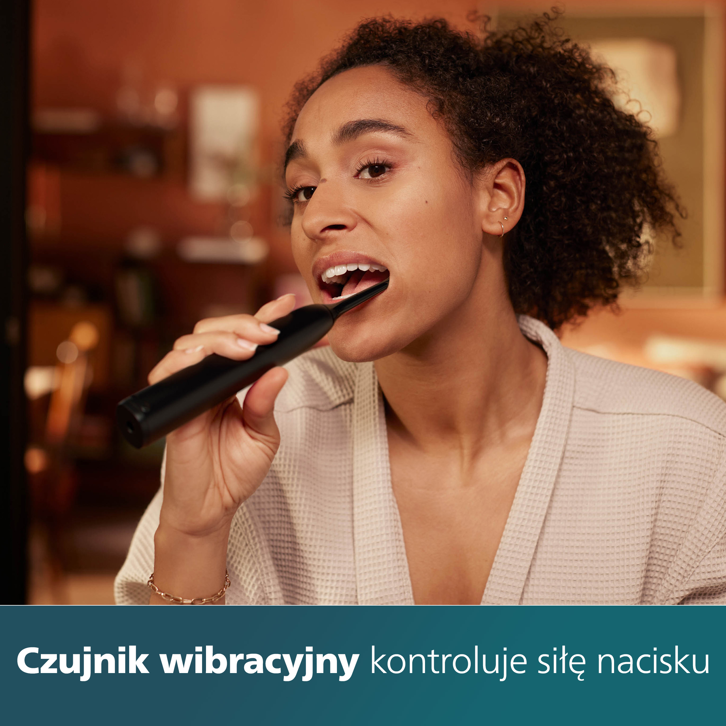 Kobieta myjąca zęby czarną szczoteczką, pokazująca jak jej używać. Jasne tło.