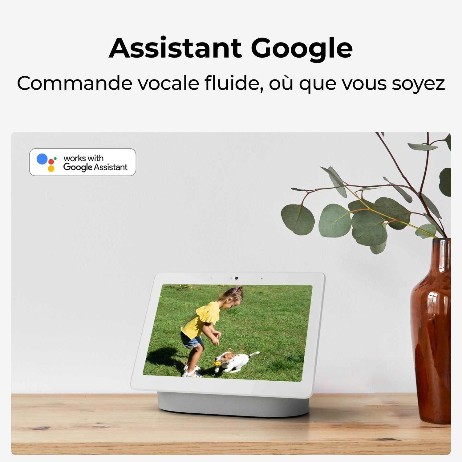 Une tablette affiche une fillette jouant. Un vase avec une plante est à côté, sur une table en bois.