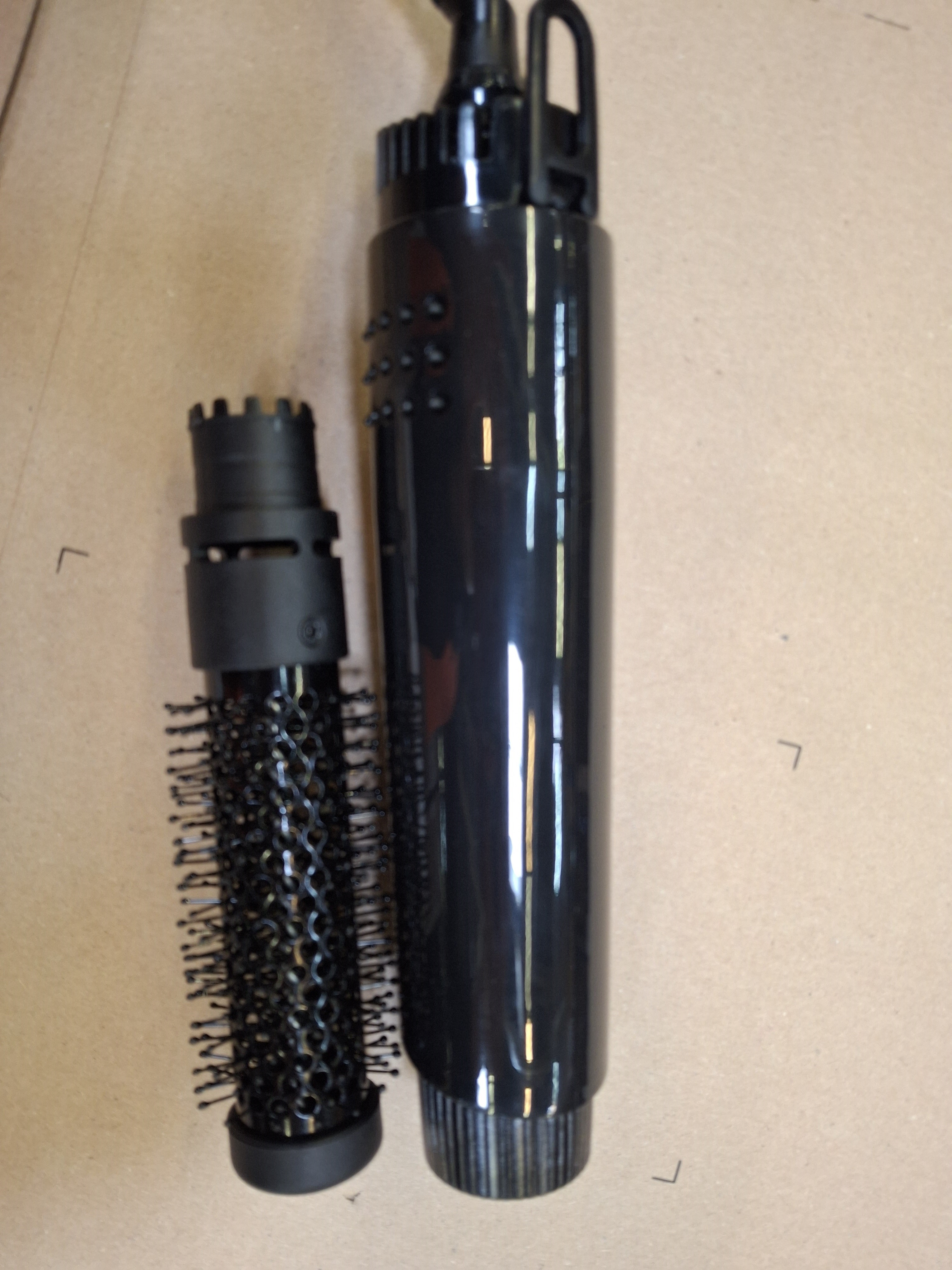 Czarny przyrząd do stylizacji włosów z dwoma nasadkami do szczotki, leżący na płaskiej powierzchni.