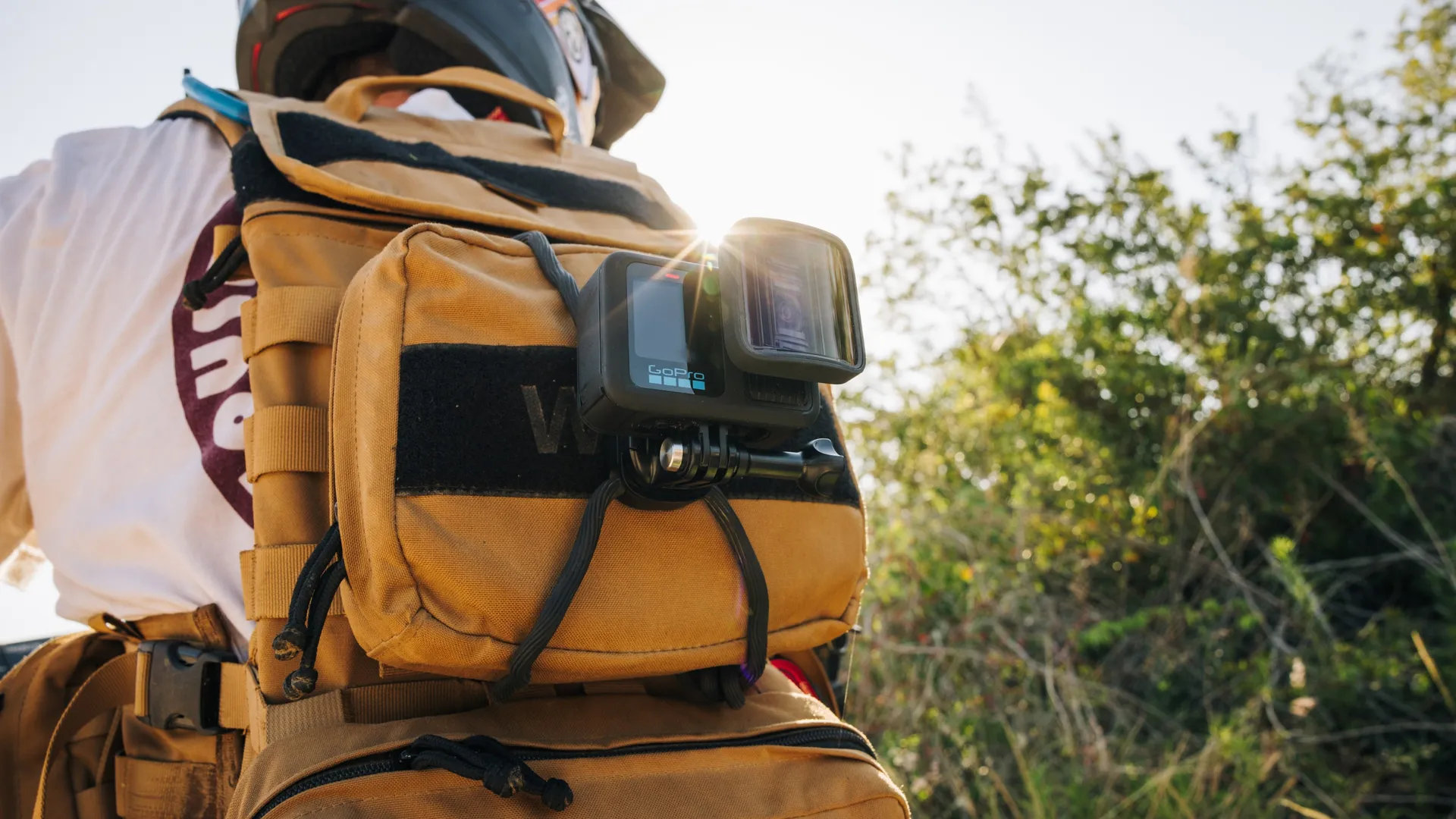 Kamera GoPro zamontowana na plecaku. Słońce świeci. Tło to zielone pole.