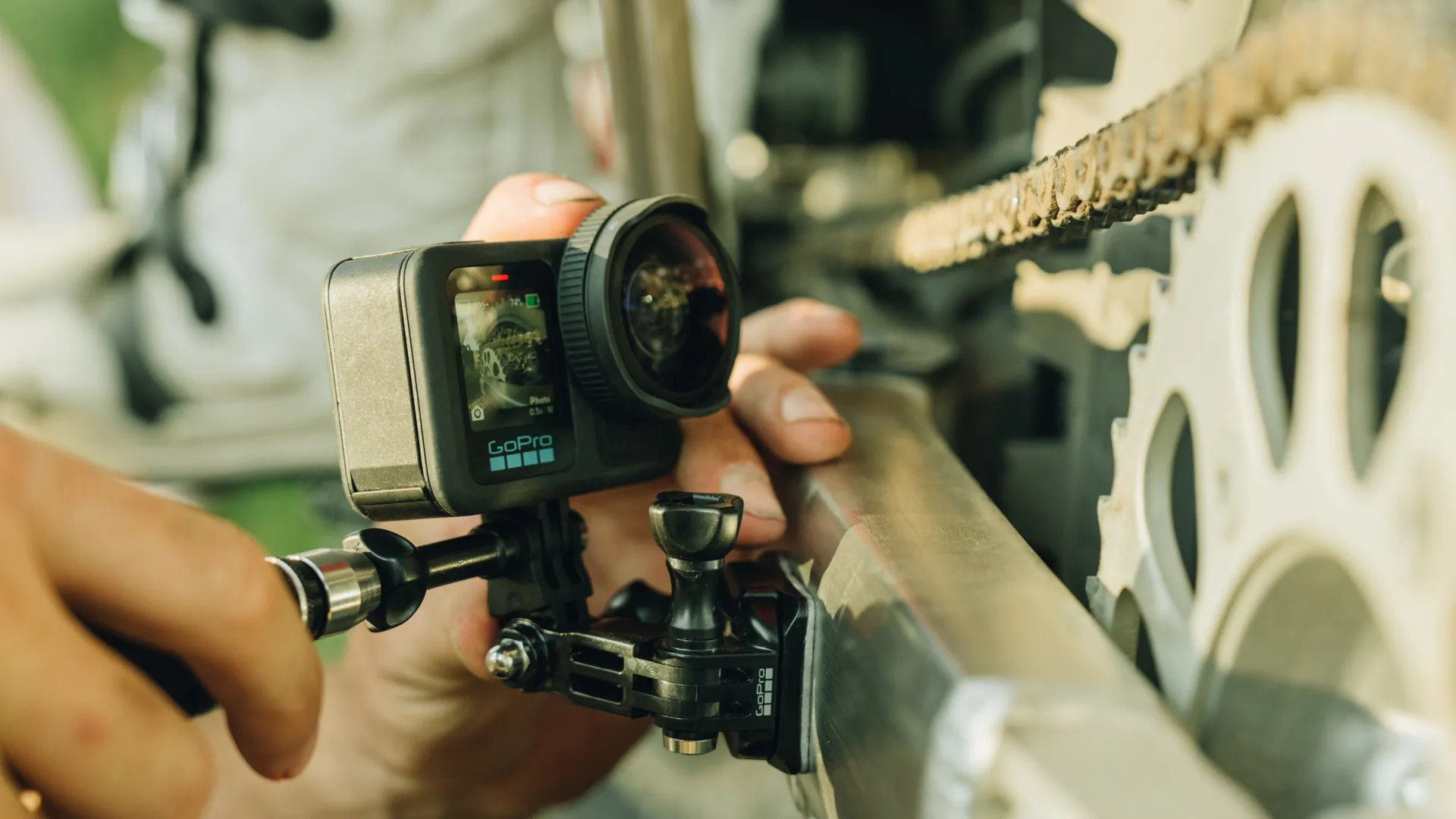 Kamera GoPro przymocowana do metalowego pręta. Ekran wyświetla obraz. Ręka trzyma kamerę.