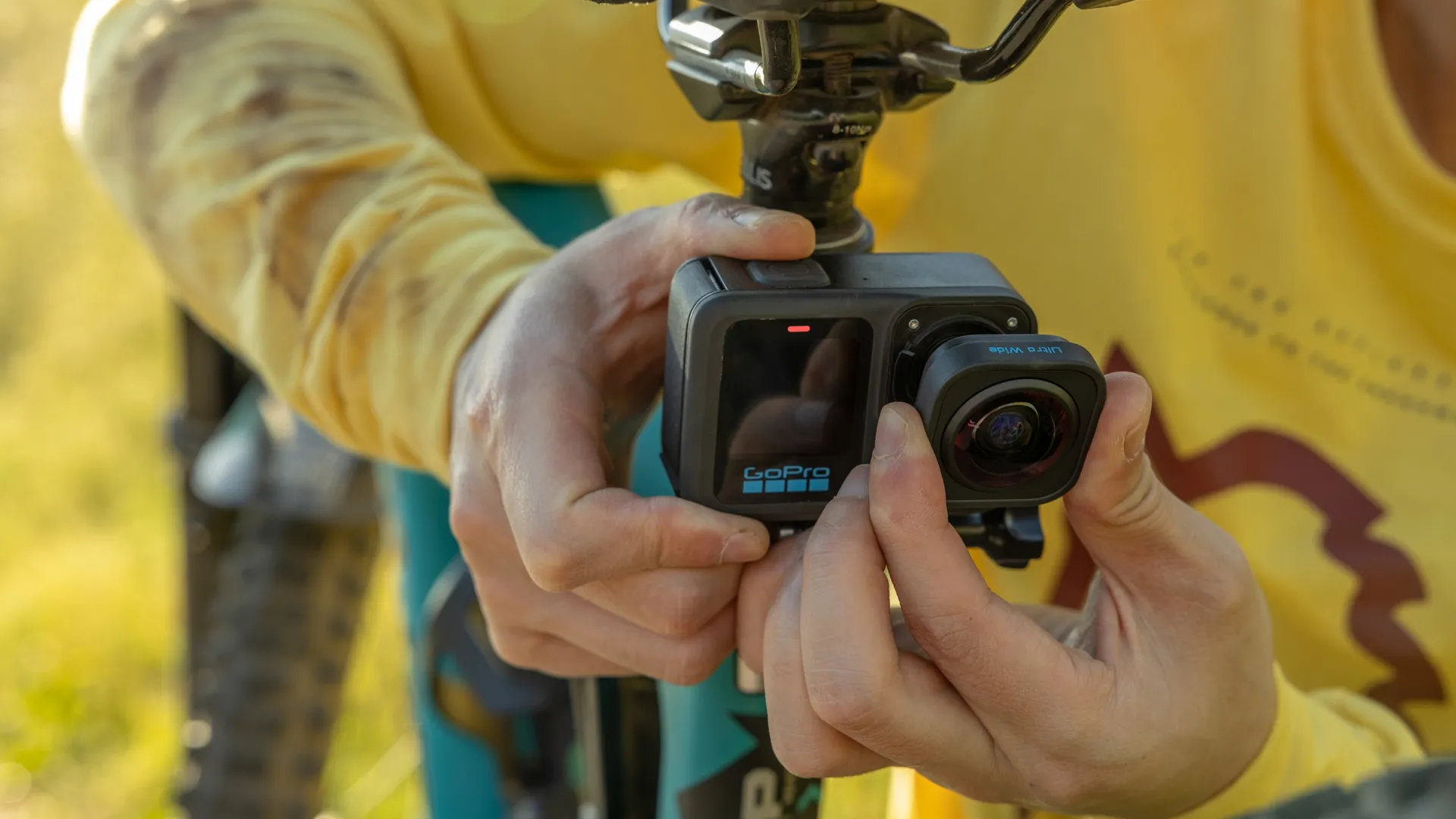 Osoba trzyma kamerę GoPro. Kamera jest zamontowana na rowerze. Żółta koszula.