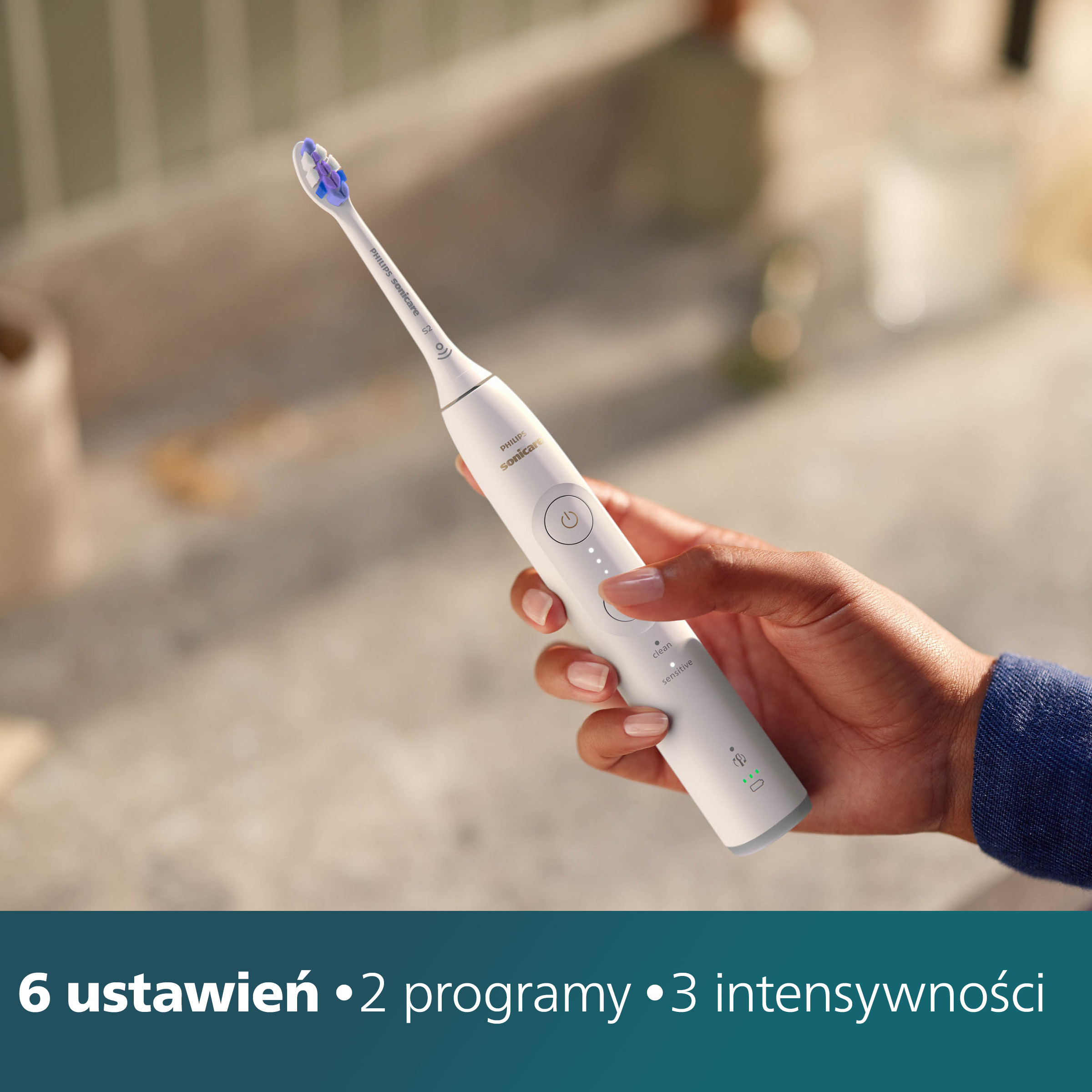 Dłoń trzyma białą szczoteczkę do zębów, pokazując przyciski sterowania i ustawienia.