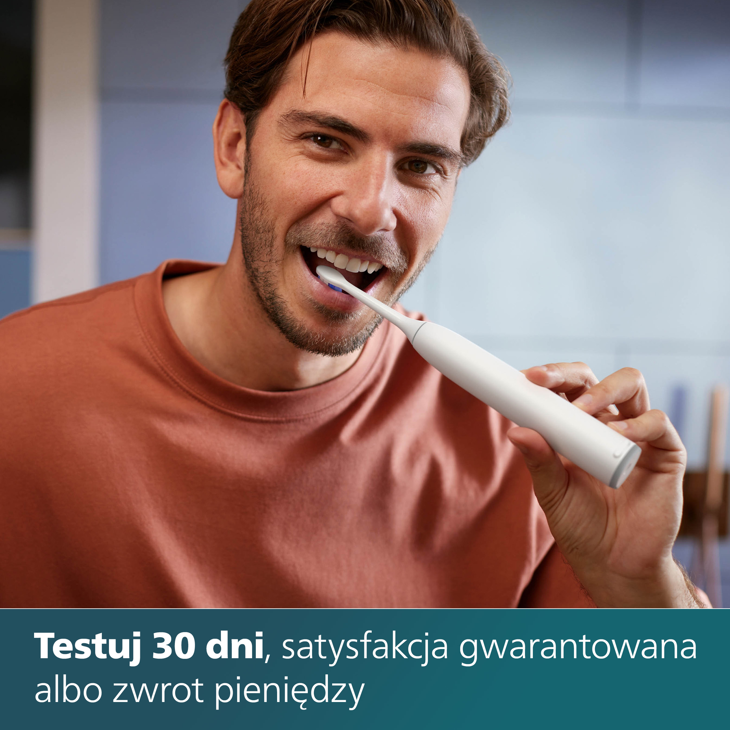 Mężczyzna uśmiecha się, myjąc zęby białą szczoteczką, pomarańczowa koszula.