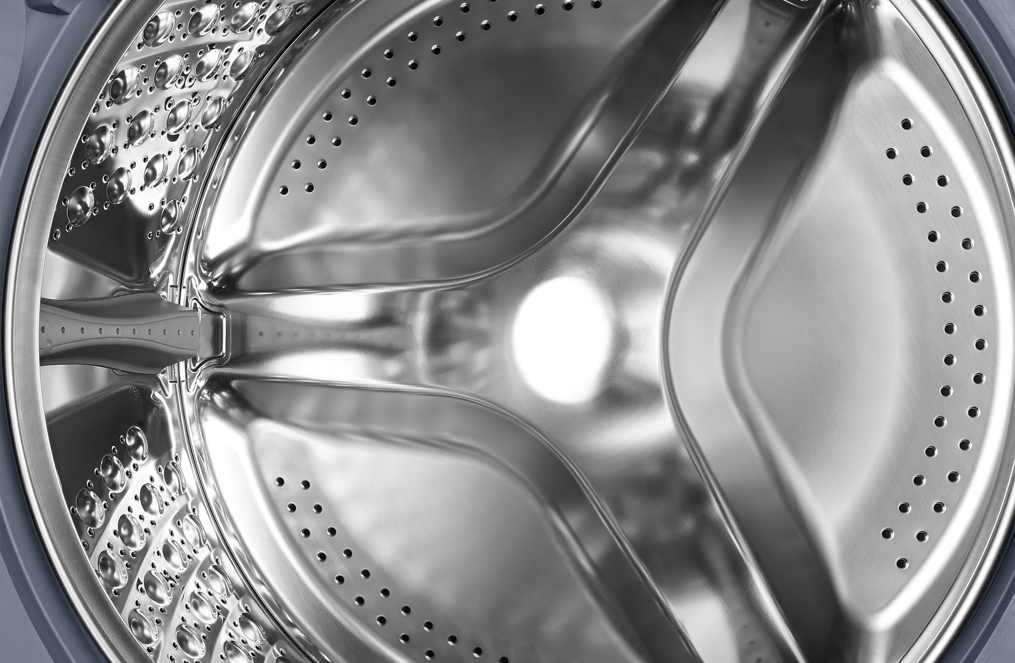 Közelkép egy ezüst mosógép dob belsejéről, lyukakkal.