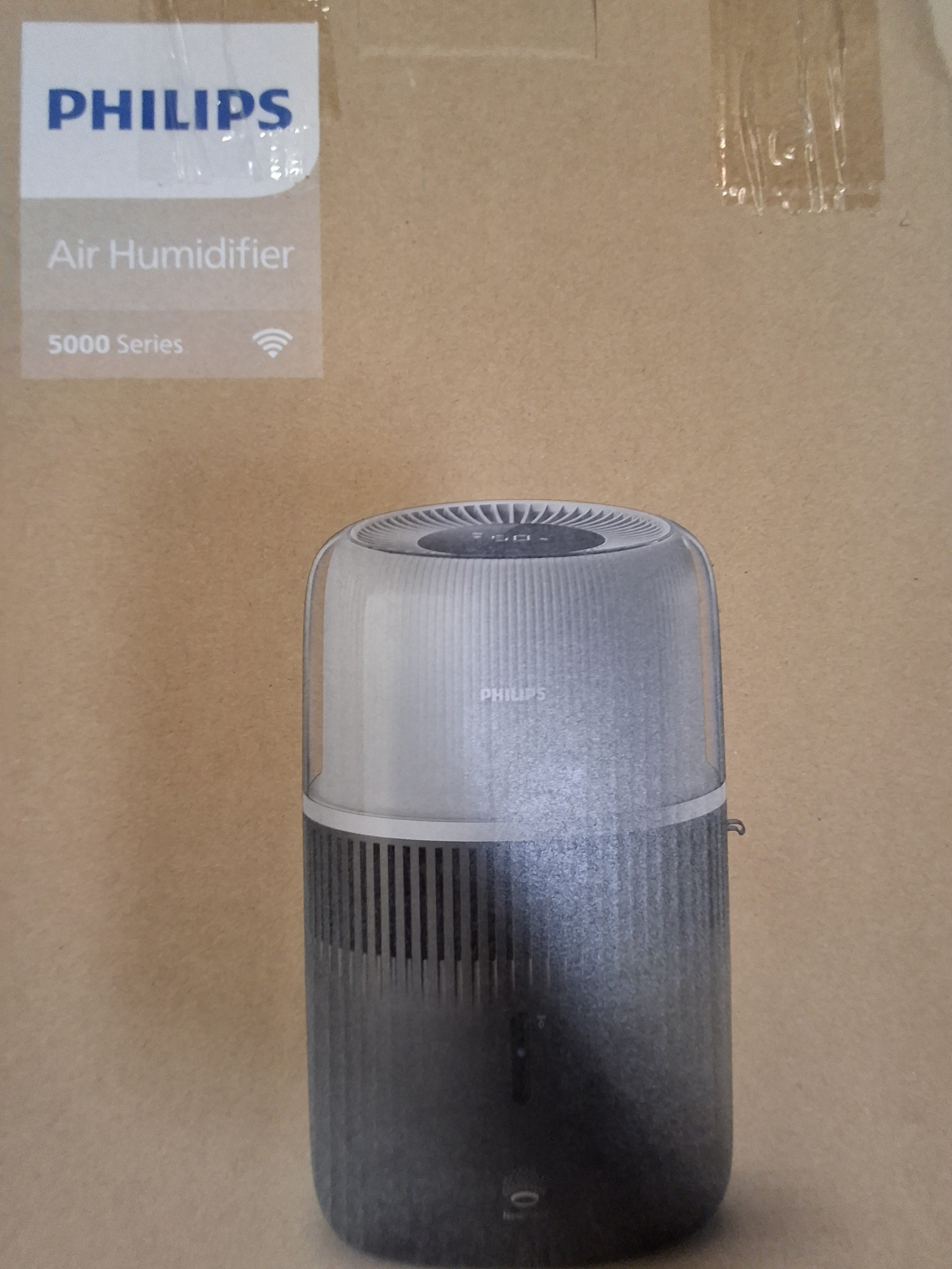 Nawilżacz powietrza Philips na tle kartonu. Urządzenie jest szare i ma cylindryczną konstrukcję.