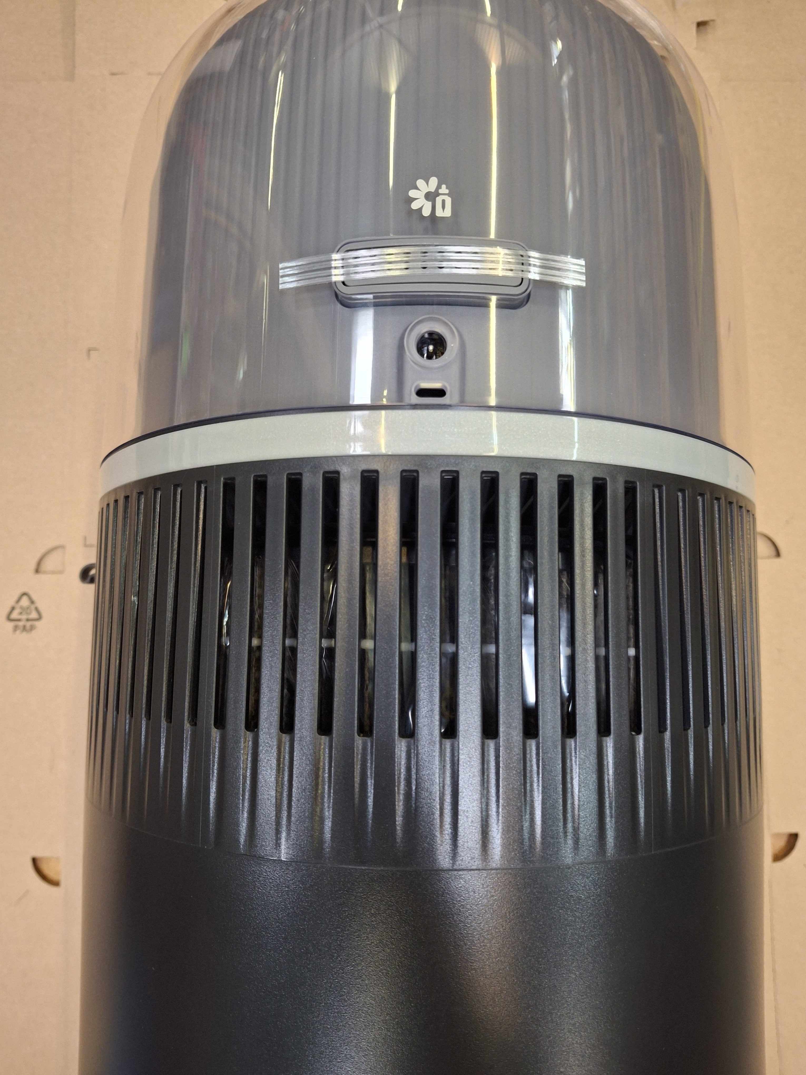 Szary oczyszczacz powietrza. Ma przezroczysty wierzch, szczelinową środkową część i czarną podstawę.