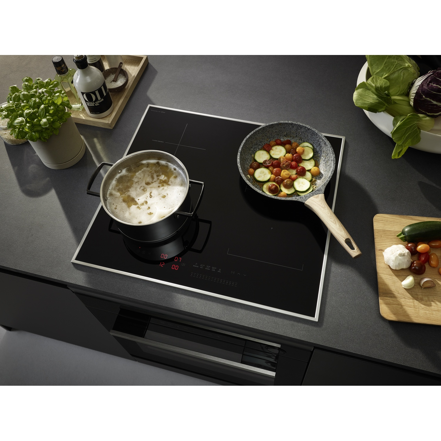 Piano cottura nero con pentola e padella. Ingredienti e cibo in entrambi.