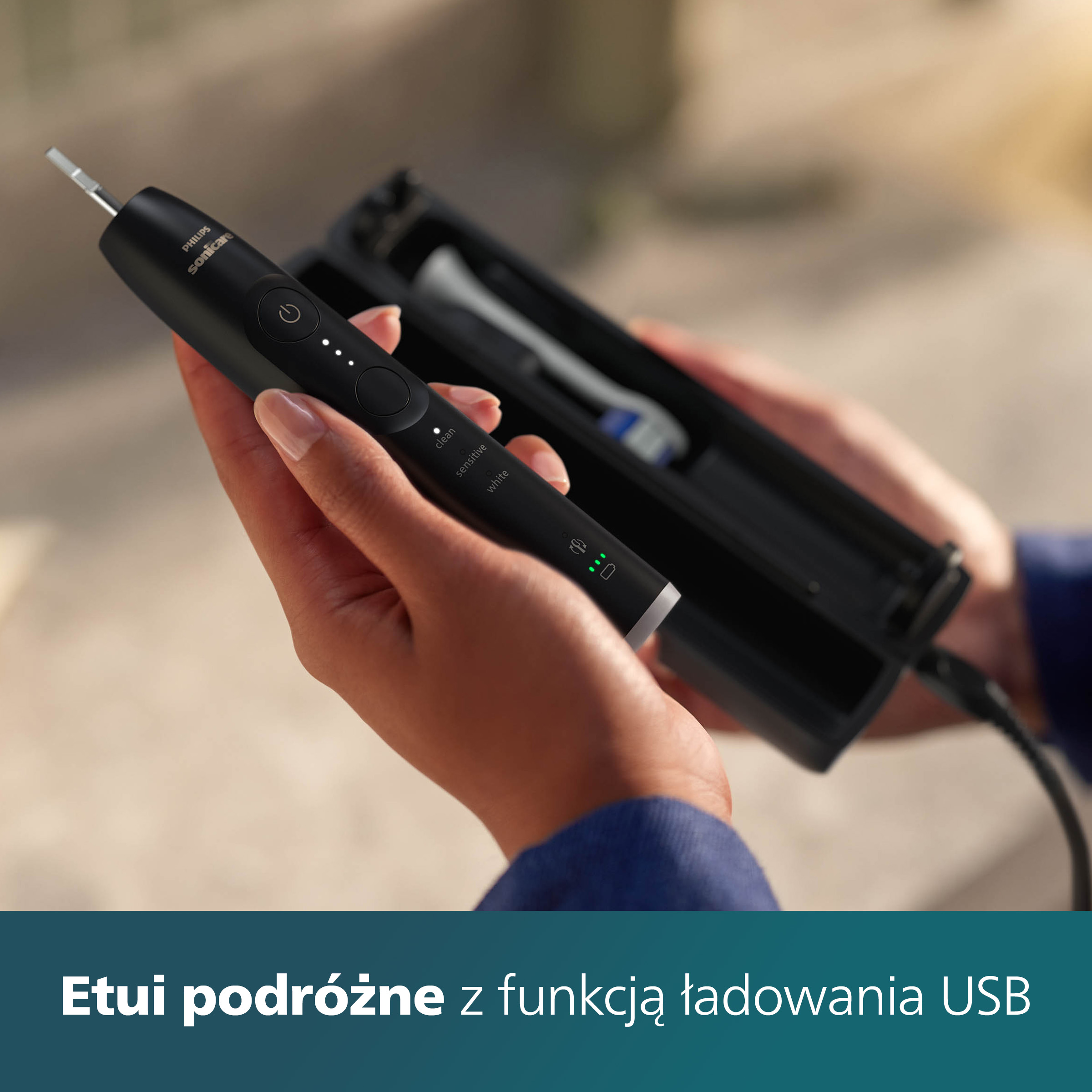 Dłoń trzyma czarną szczoteczkę Philips Sonicare i etui podróżne z ładowaniem. Rozmyte tło.