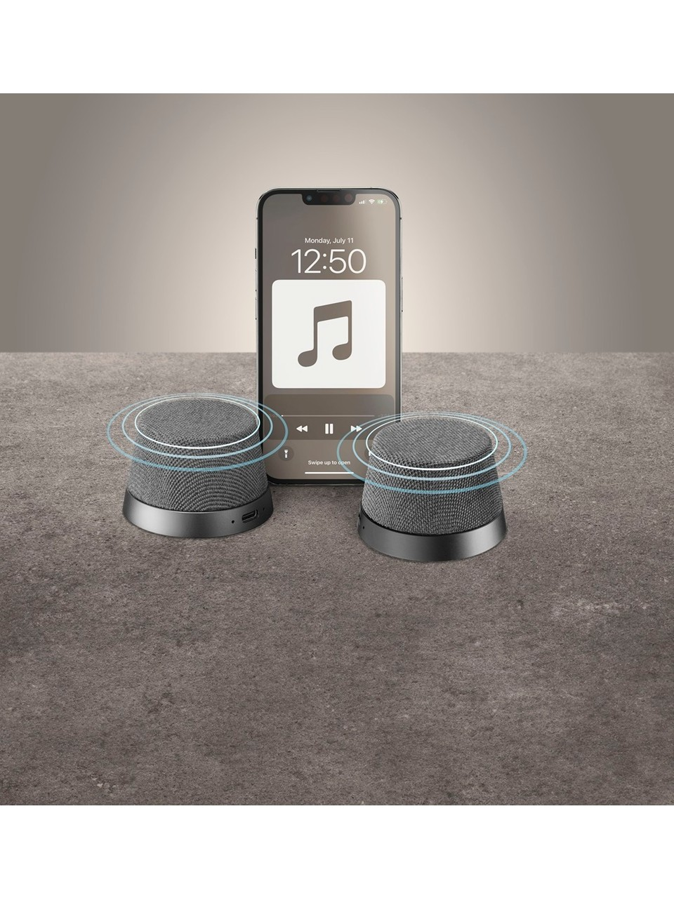Gri bir yüzeyde müzik uygulaması gösteren bir telefonla birlikte iki küçük hoparlör.