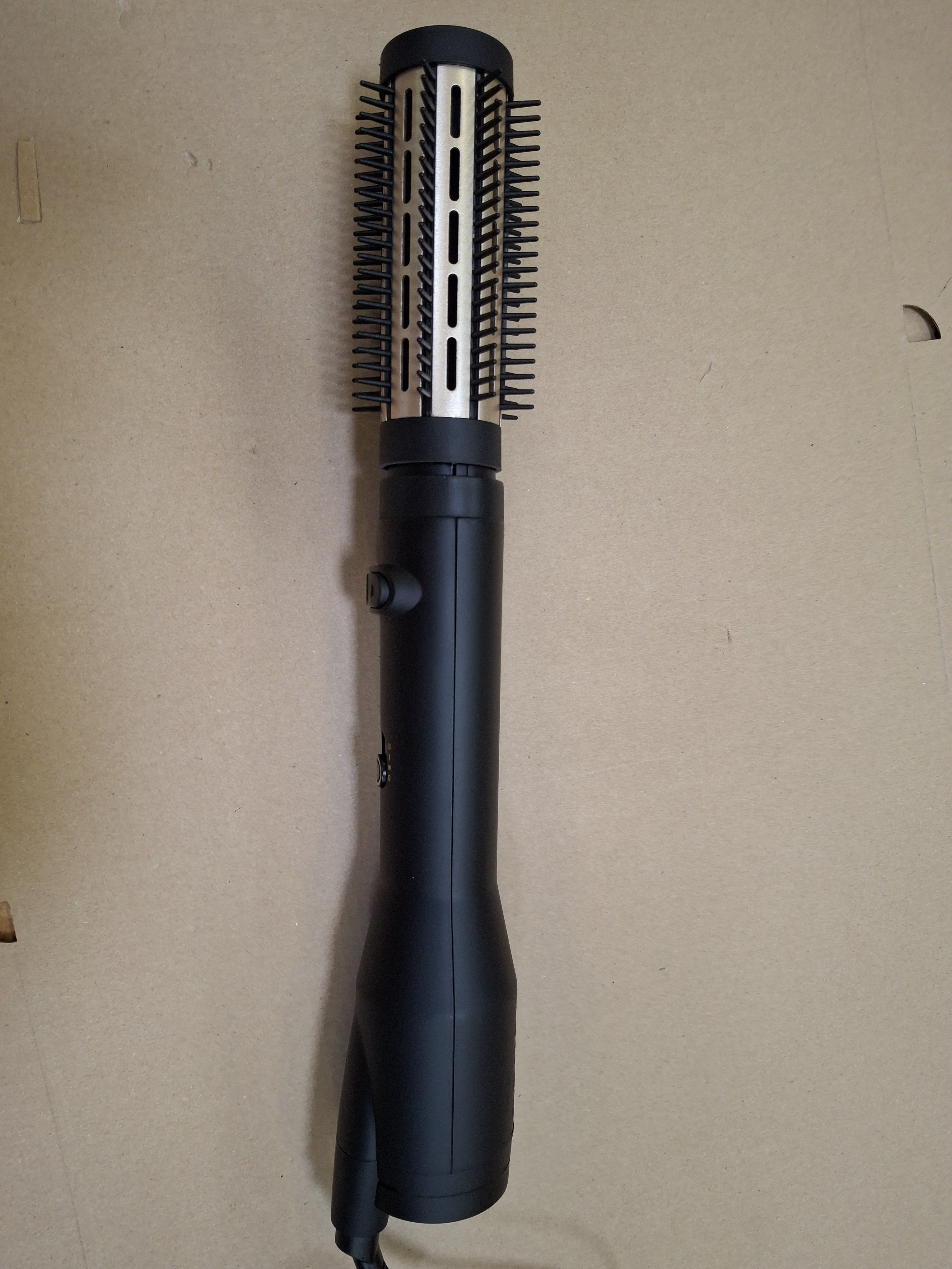 Zbliżenie czarnego narzędzia do stylizacji włosów. Ma uchwyt i cylindryczną główkę szczotki z włosiem.