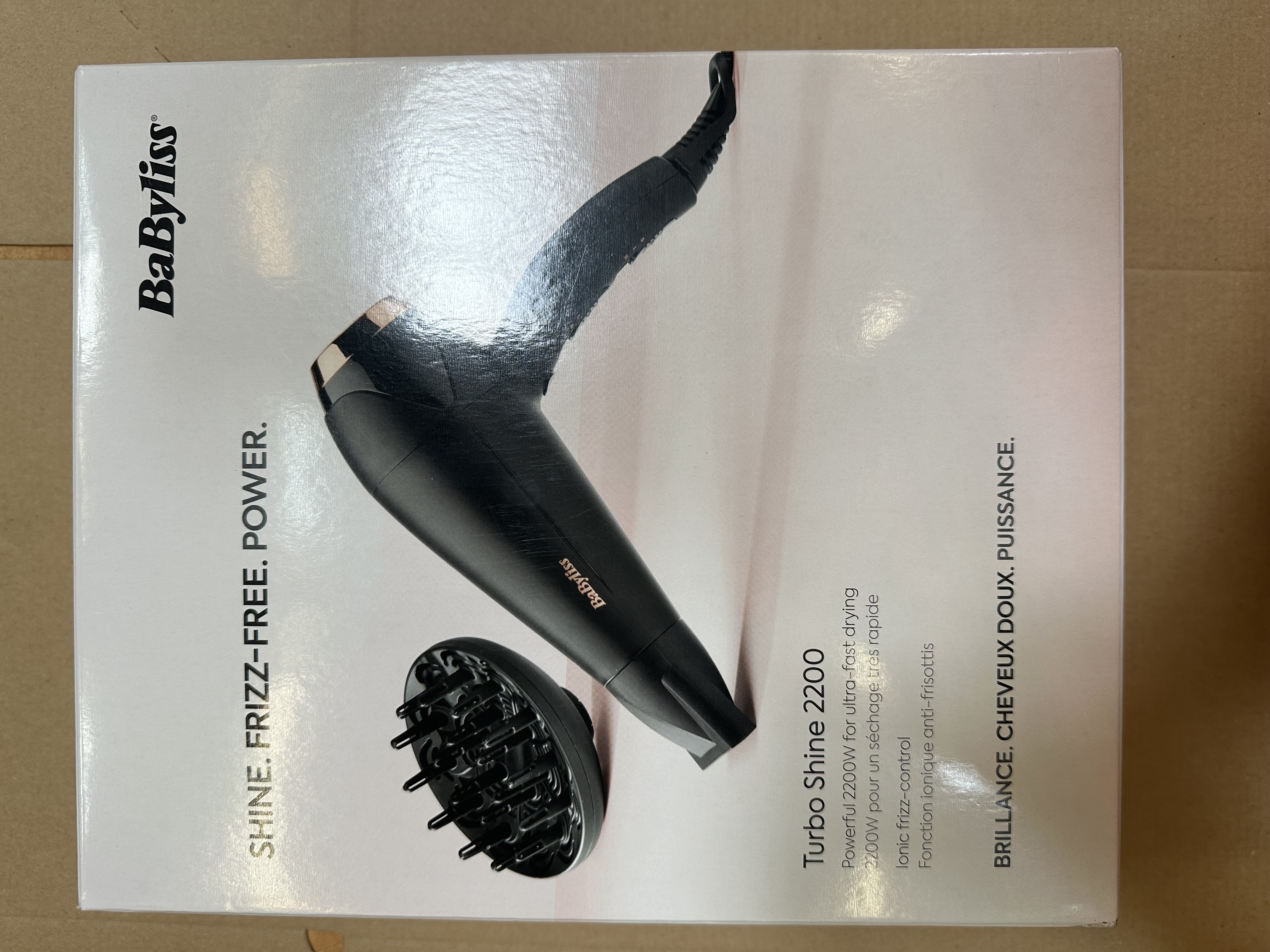 Białe pudełko z czarną suszarką do włosów w środku. Pudełko ma tekst i obrazy. Tło jest brązowe.