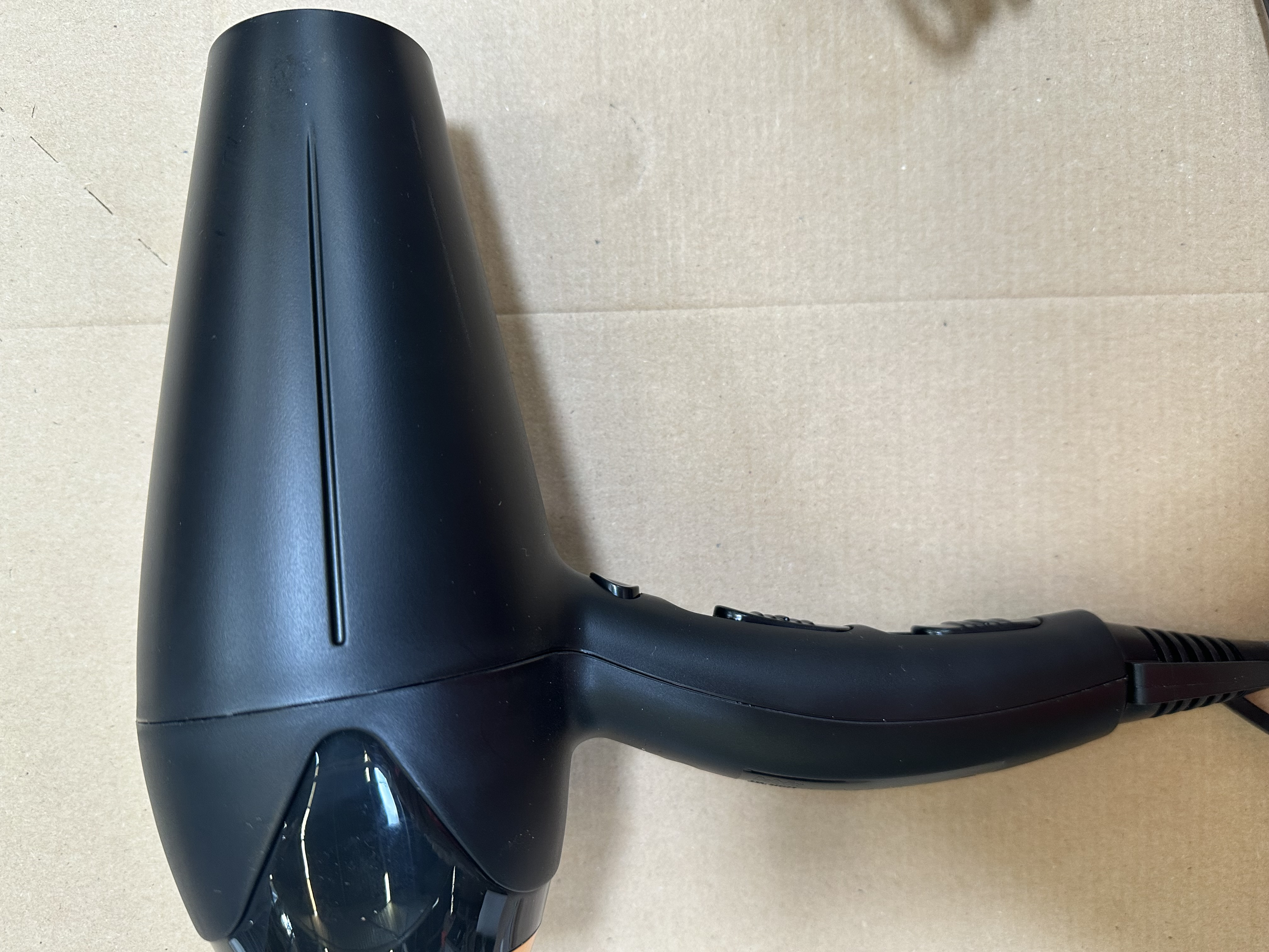 Czarna suszarka do włosów leży na brązowej powierzchni. Suszarka ma uchwyt i dyszę. Tło jest gładkie.