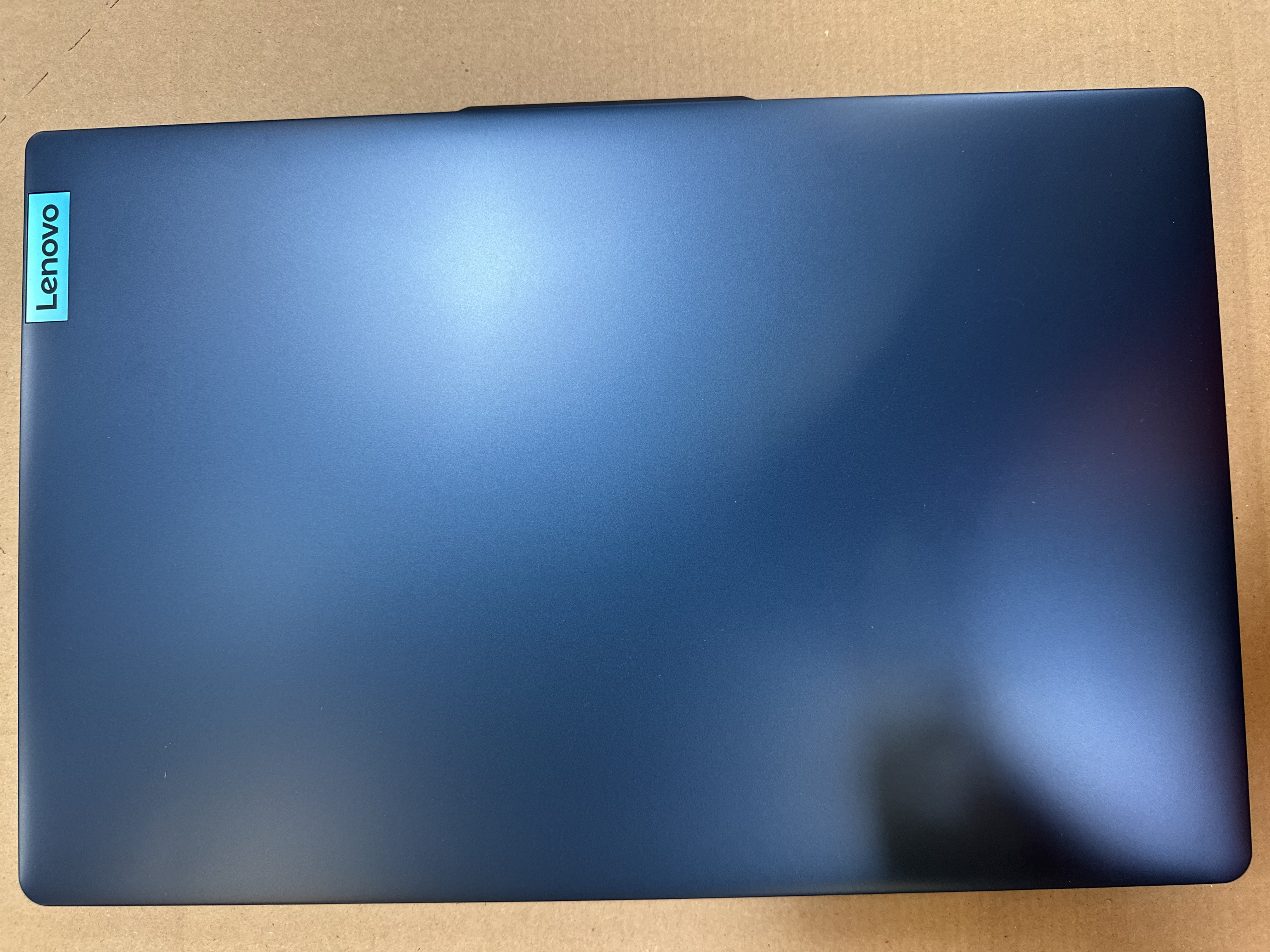 Zamknięty niebieski laptop z naklejką Lenovo. Powierzchnia gładka i metaliczna.