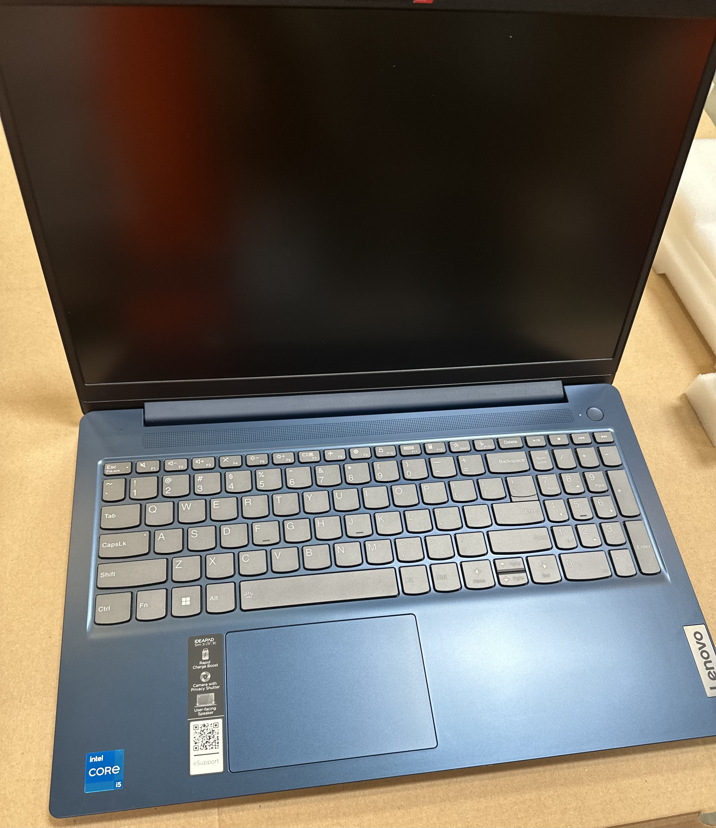 Niebieski otwarty laptop na brązowej powierzchni. Widoczna klawiatura i ekran.