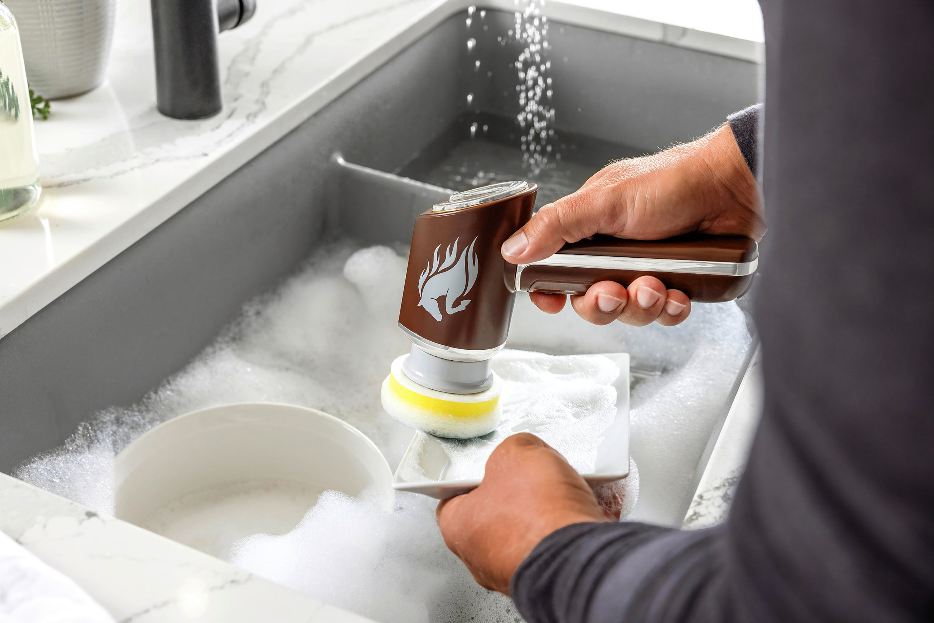 Eine Person reinigt Geschirr mit einem Reinigungswerkzeug in einem Waschbecken mit Wasser und Seife.