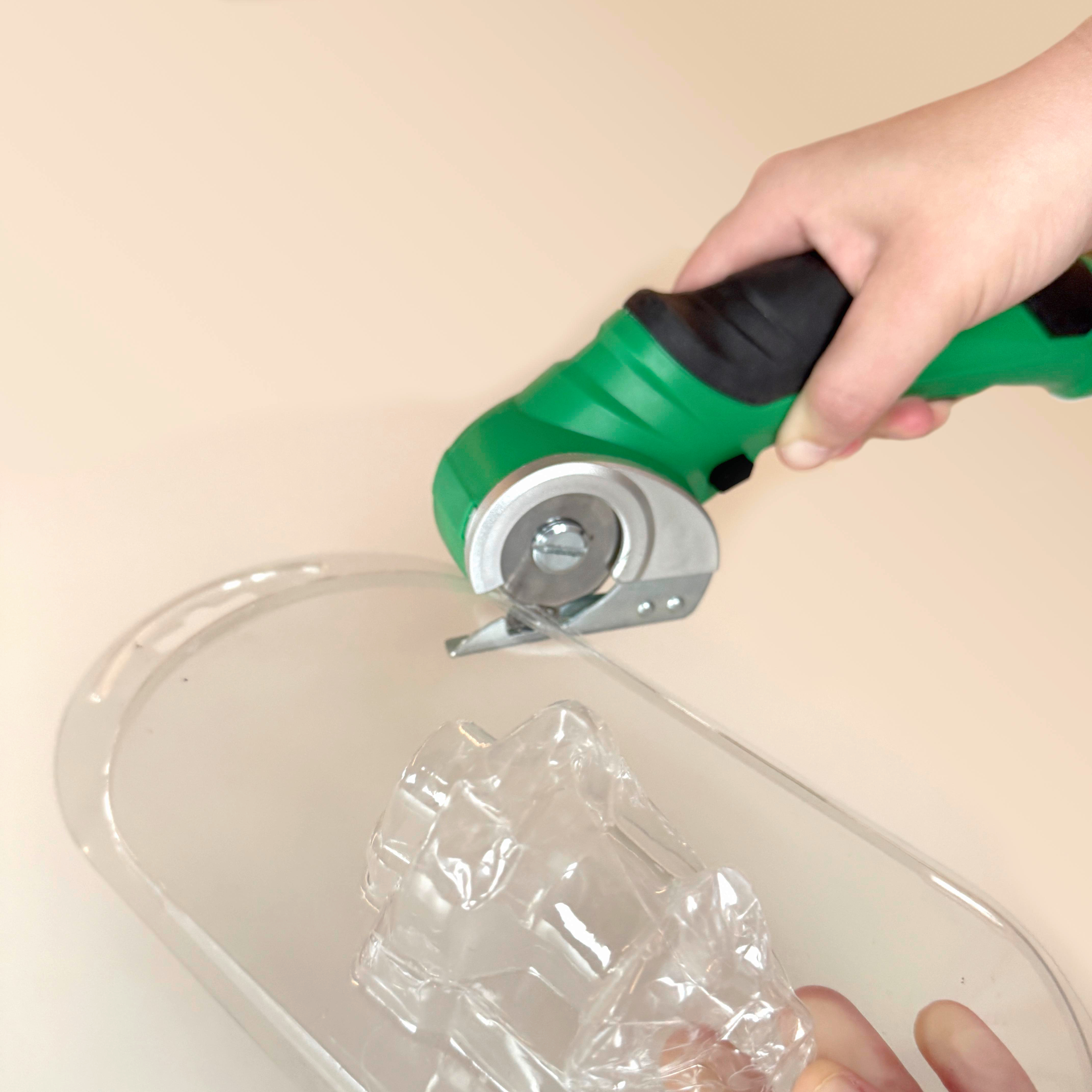 Hand, die einen grünen Cutter auf einem Plastikbehälter verwendet. Beige Oberfläche, Nahansicht.