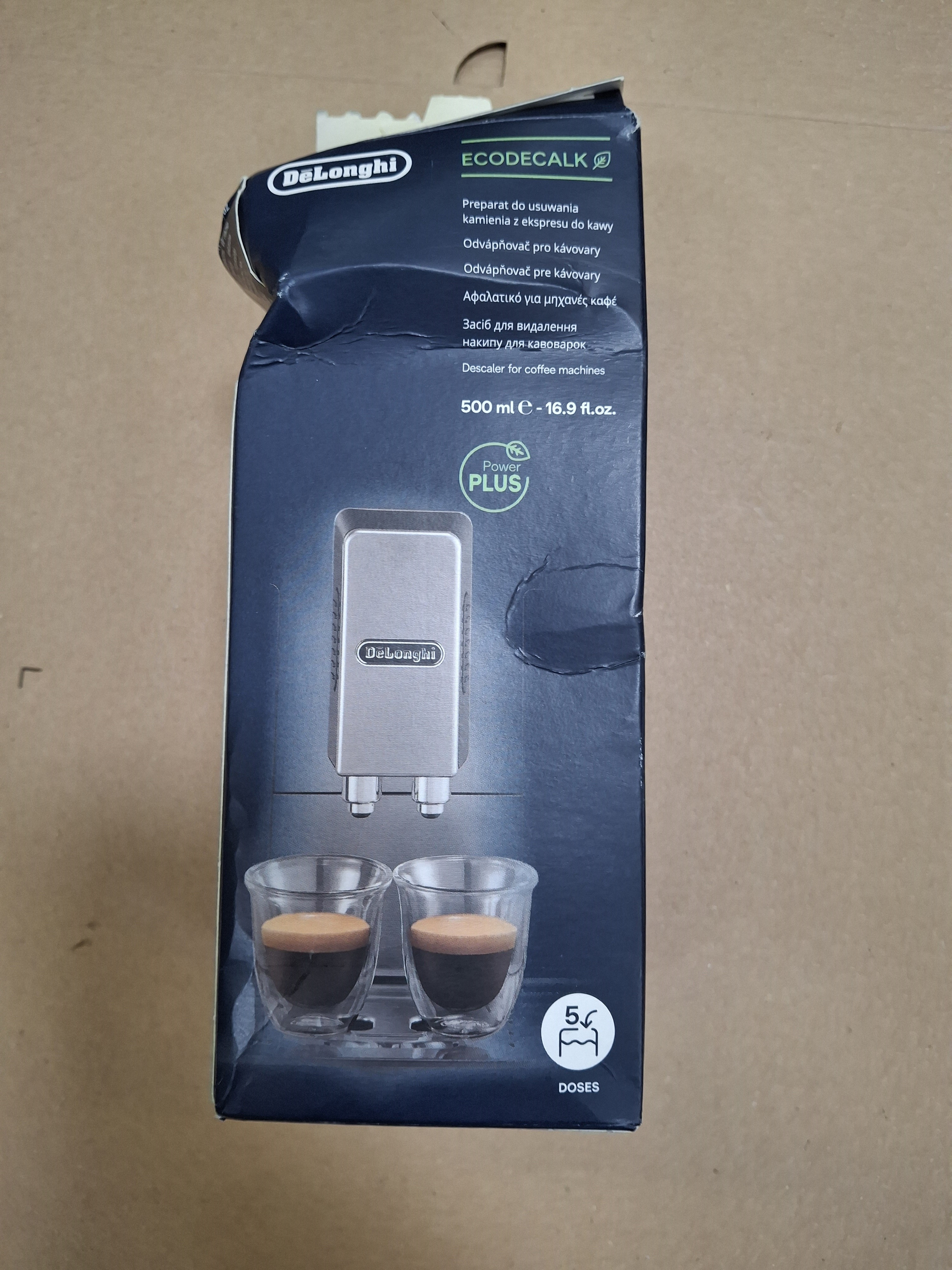 Pudełko ekspresu do kawy DeLonghi, z filiżankami i obrazem srebrnej maszyny.