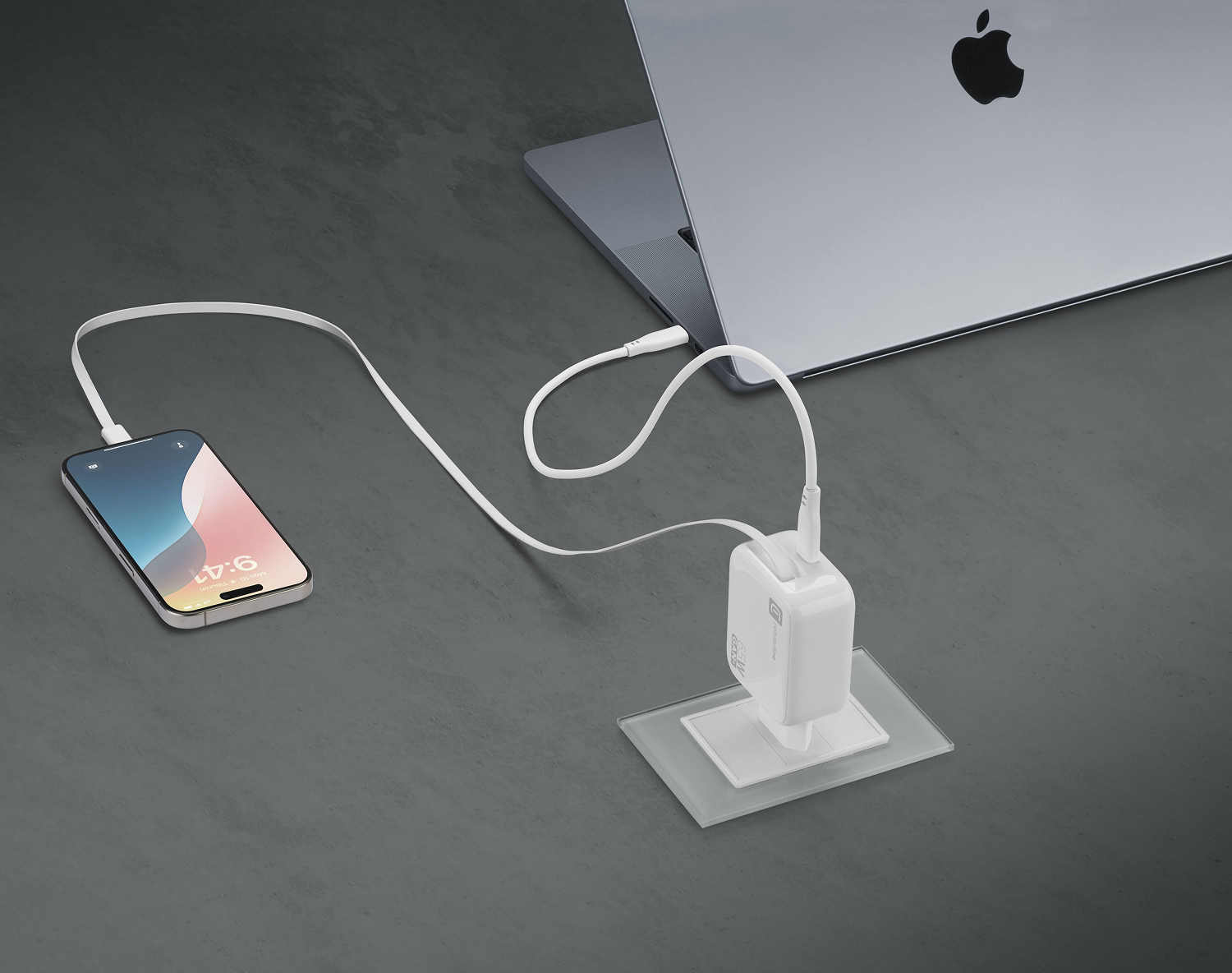 Teléfono cargando en un escritorio con un portátil. Un cargador y cable blancos conectan el teléfono y el portátil.