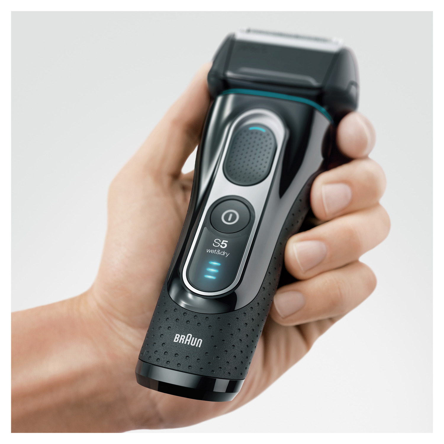 A hand holding a black Braun Series 5 wet & dry shaver, against a light background.