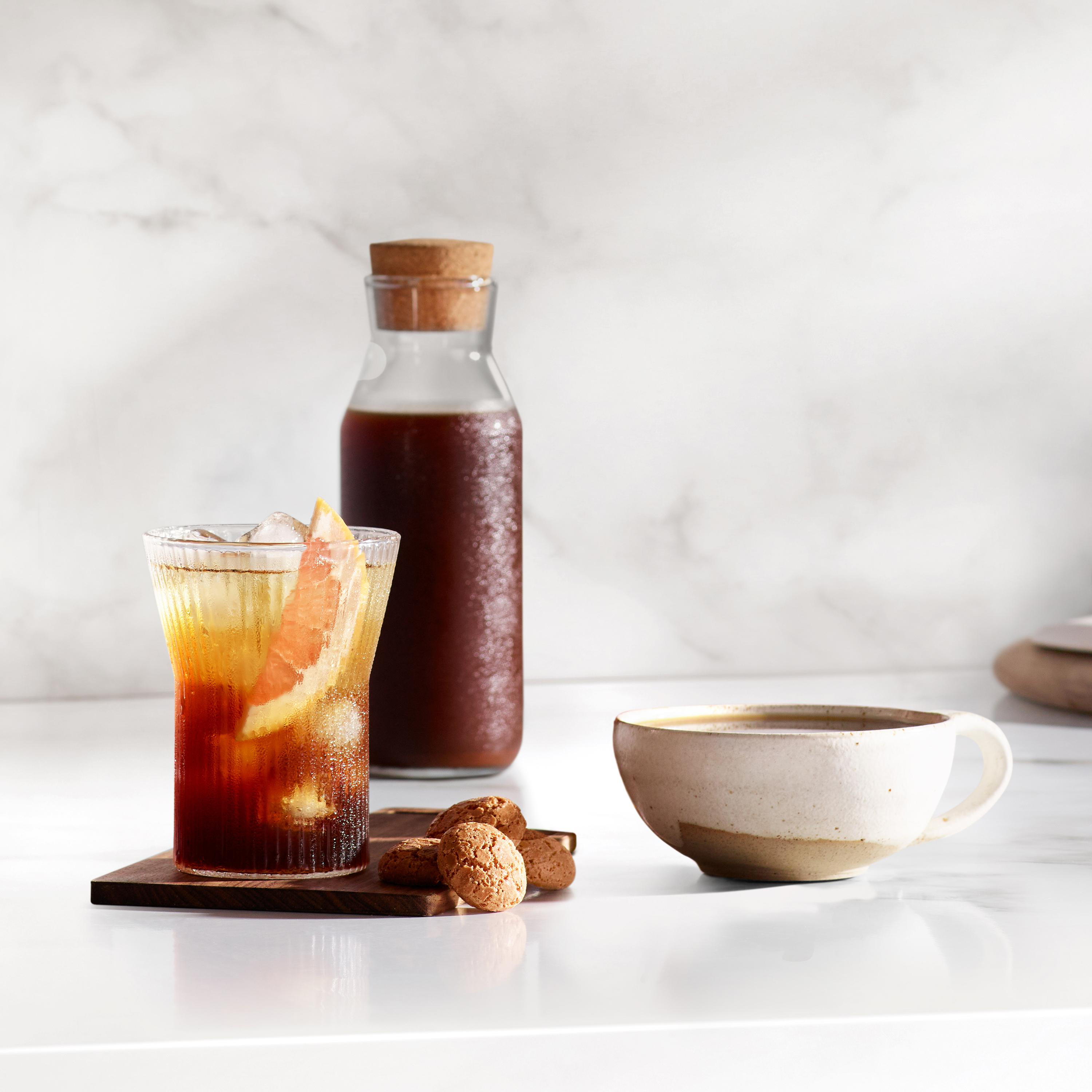 Glas mit Eistee, Grapefruit, Flasche, Keksstapel und Kaffeetasse auf weißem Tisch.