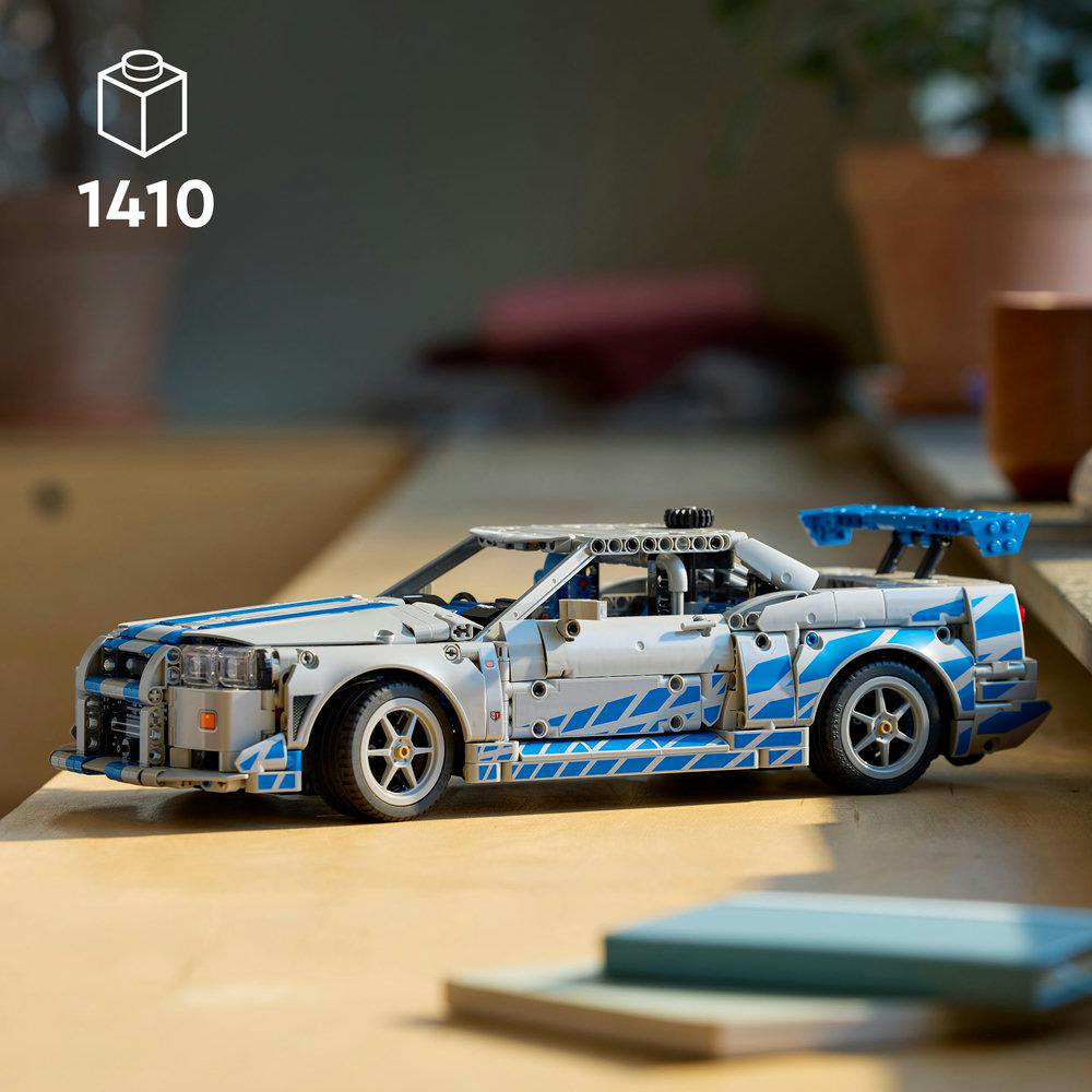 Ein silber-blaues Lego-Auto steht auf einem Tisch. Im Hintergrund ein Stapel Bücher.