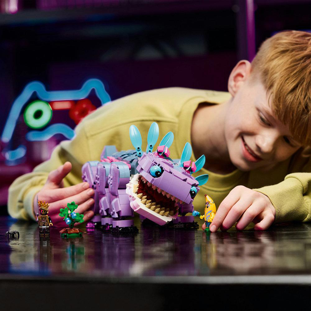 Ein Kind spielt mit einem lila LEGO-Dinosaurier, Minifiguren und einer Bananenfigur, alles auf einem Tisch.