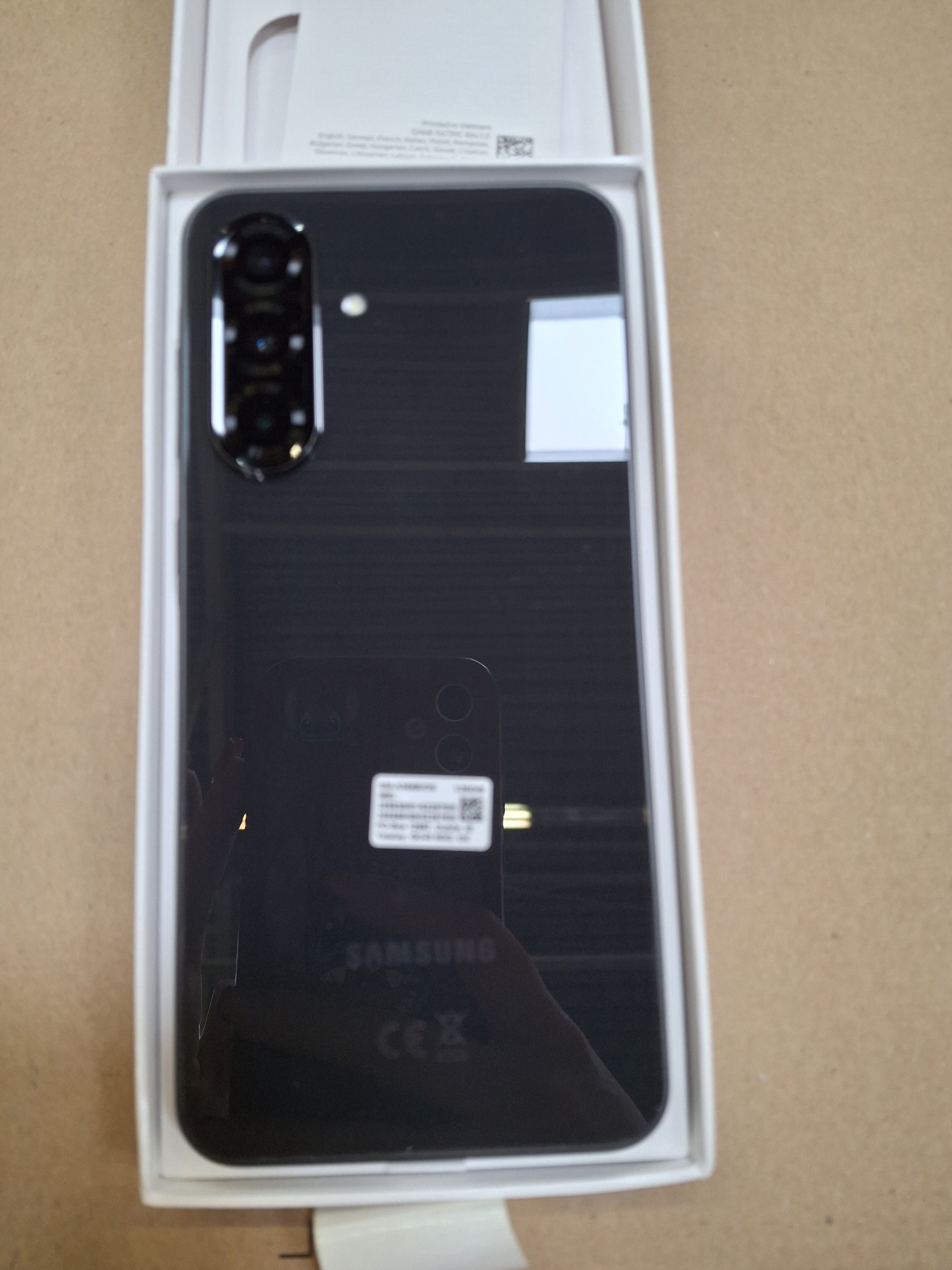 Czarny smartfon Samsung w białym pudełku. Telefon ma wiele kamer i logo Samsung z tyłu.