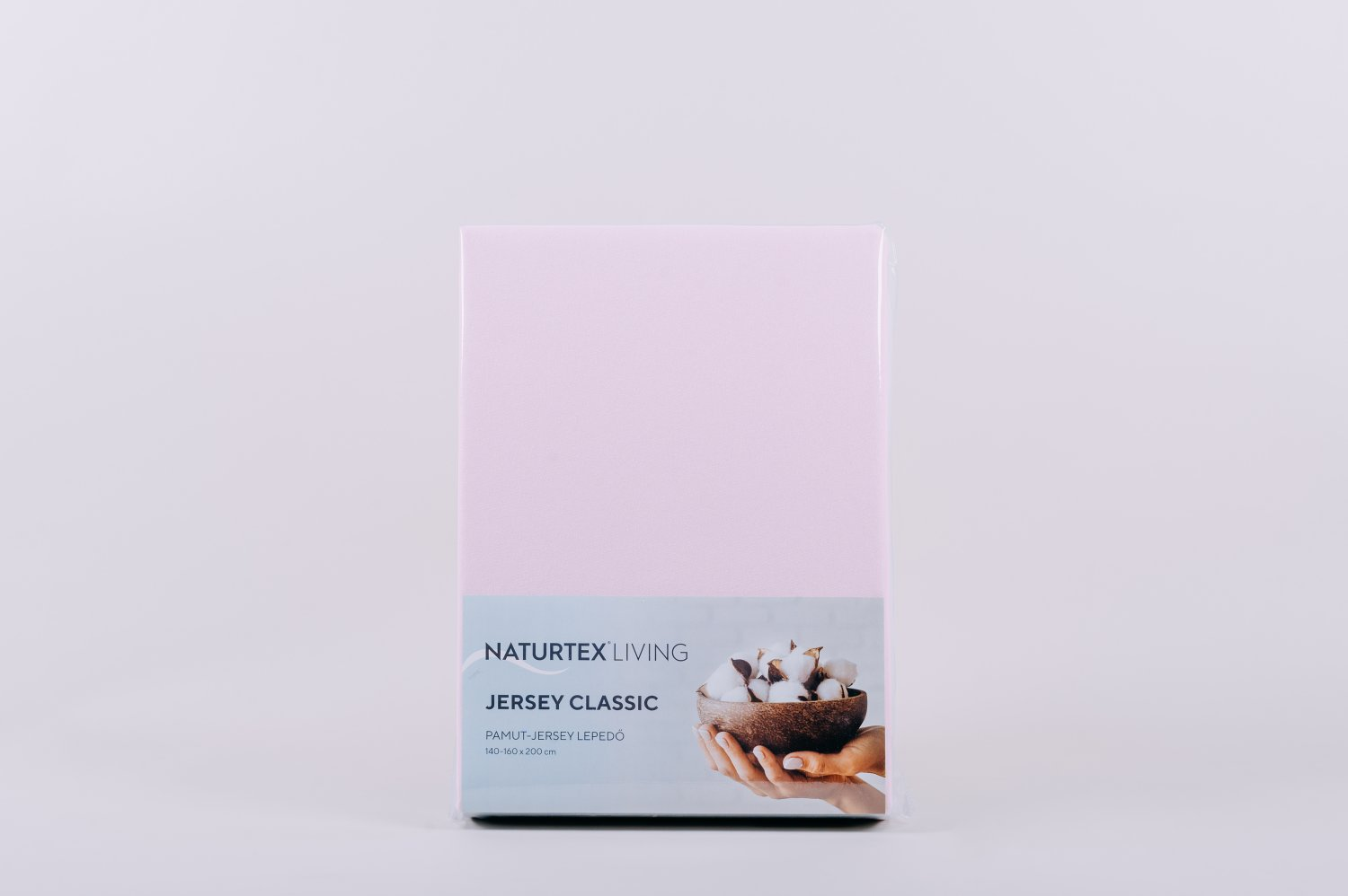 Rózsaszín lepedő csomagban. Fehér háttér. Szöveg: Jersey Classic. Kép a pamutról tálban.