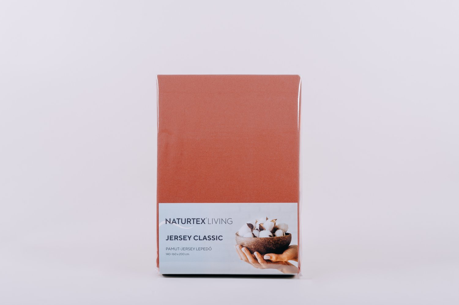 Terrakotta színű lepedő csomagban. Fehér háttér. Szöveg: Jersey Classic. Kép a pamutról tálban.