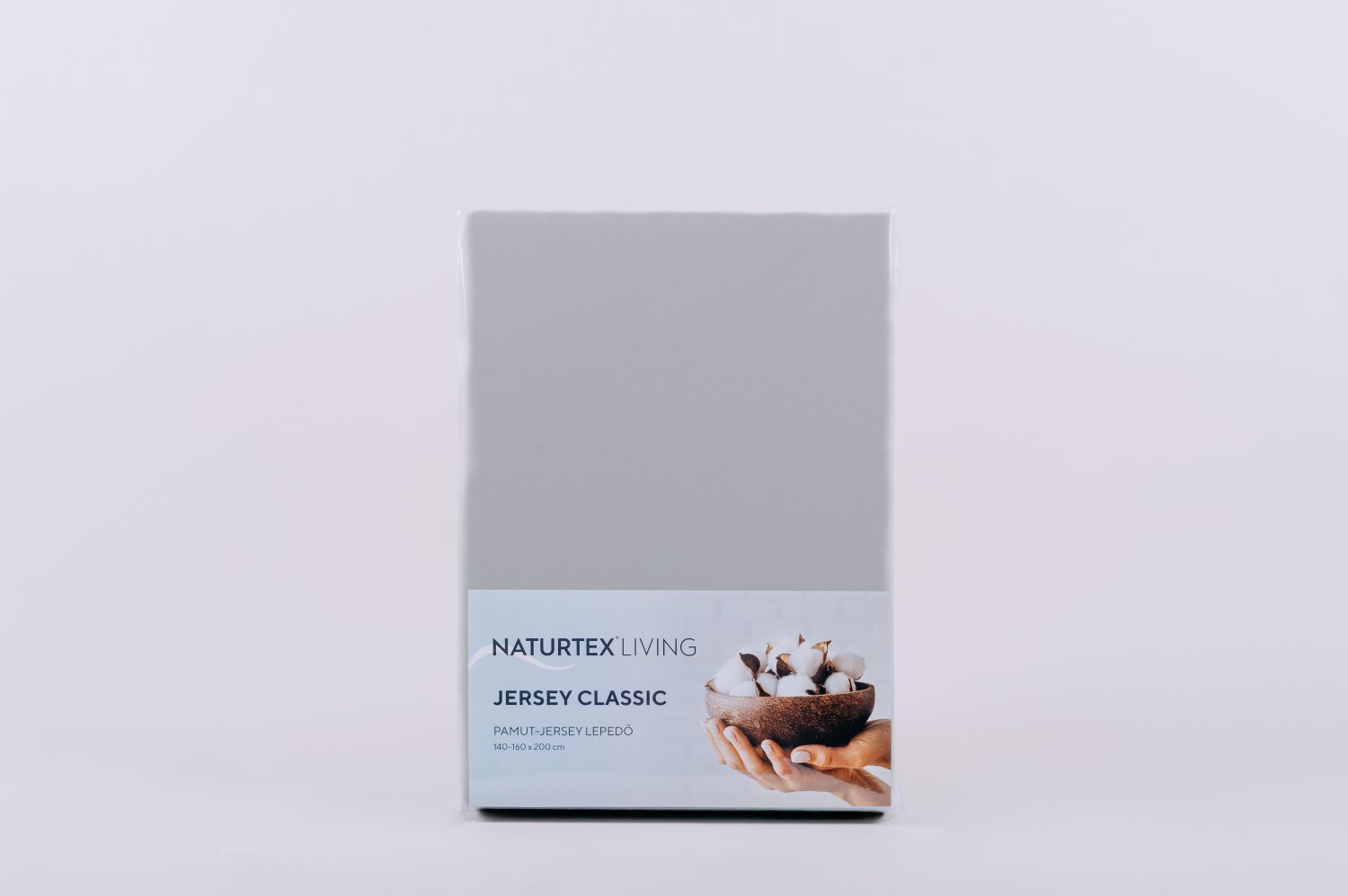 Szürke lepedő csomagban. Fehér háttér. Szöveg: Jersey Classic. Kép a pamutról tálban.