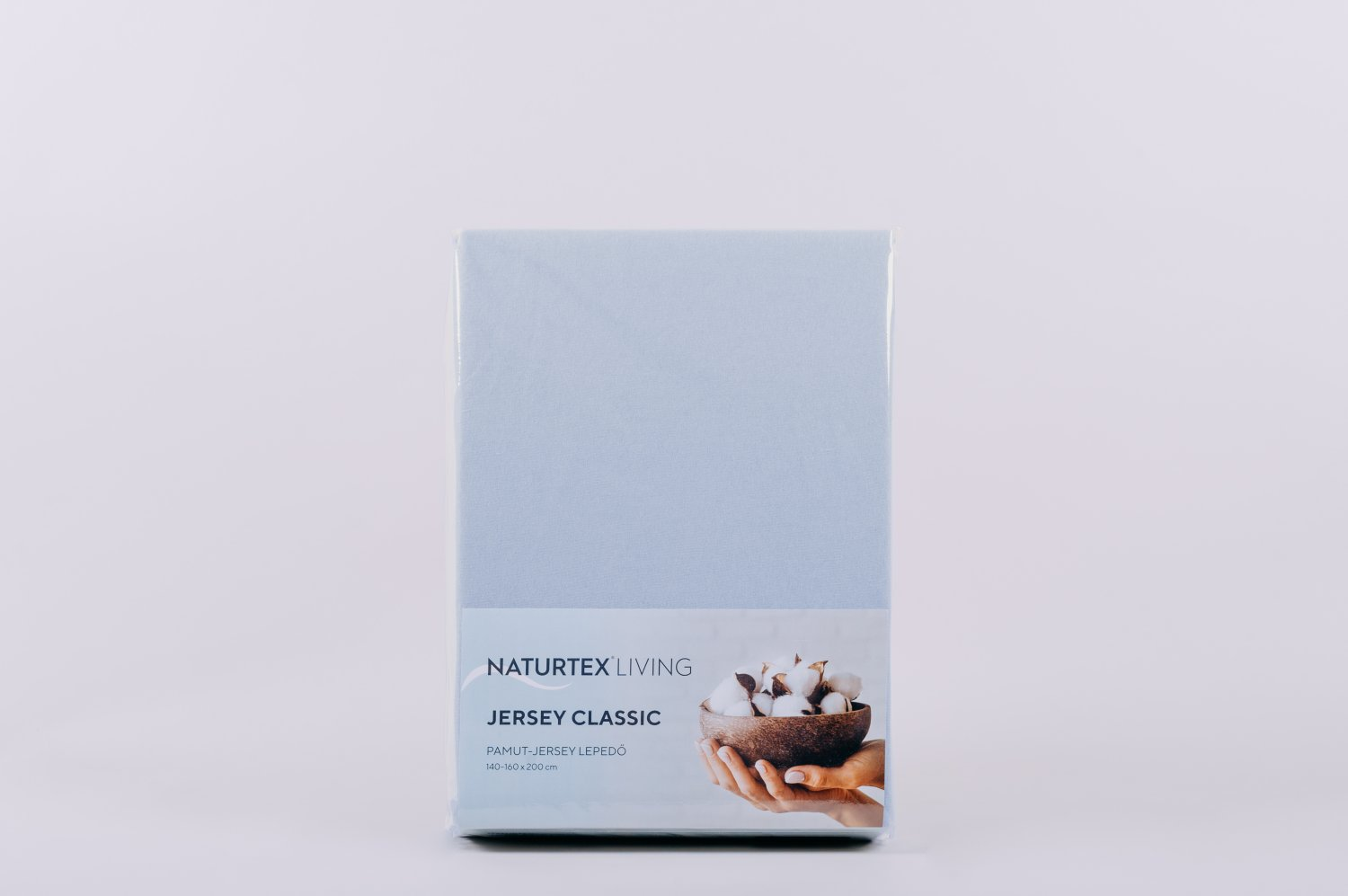 Egy világoskék Naturtex Living Jersey Classic lepedő készlet. Fehér háttér. A címke pamutot és kezet mutat.