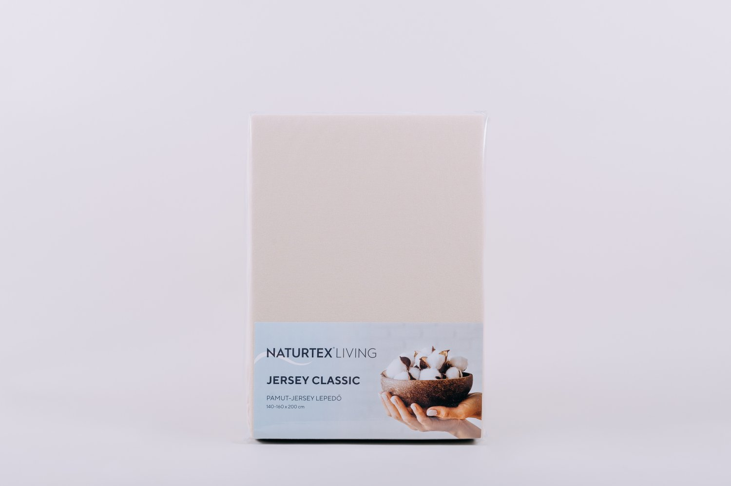 Egy bézs Naturtex Living Jersey Classic lepedőkészlet. Fehér háttér. A címke pamutot és kezet mutat.
