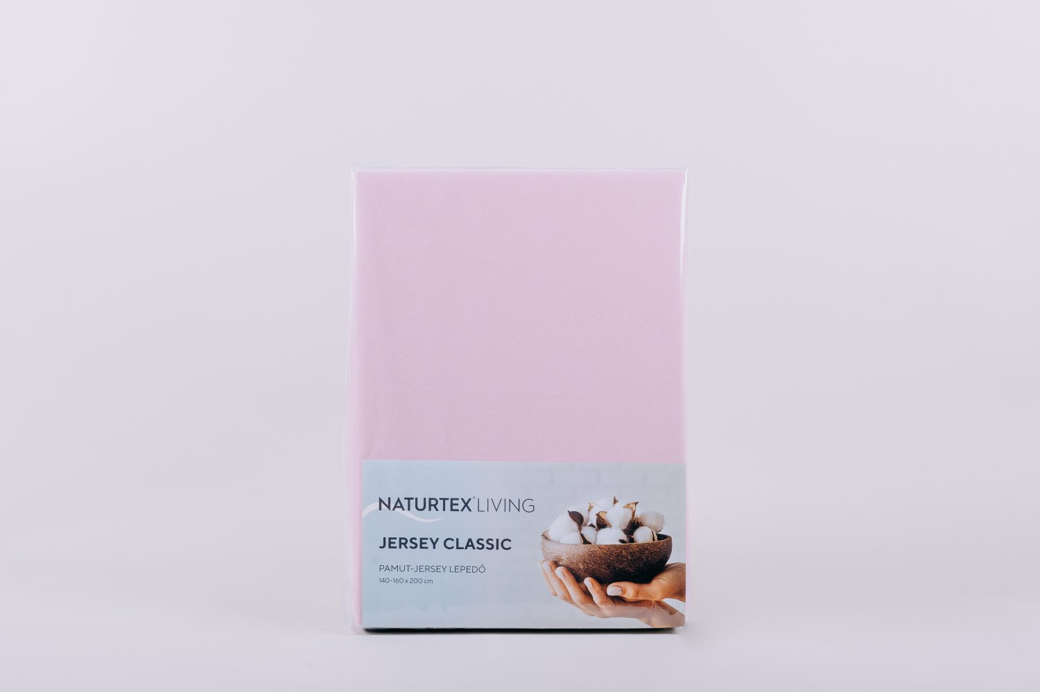 Egy rózsaszín Naturtex Living Jersey Classic lepedőkészlet. Fehér háttér. A címke pamutot és kezet mutat.