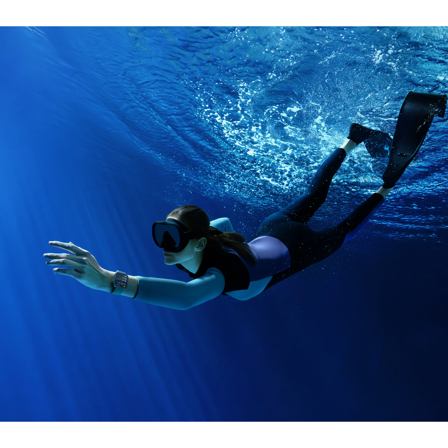 Woman diving underwater with snorkel gear. Wearing a wetsuit and smartwatch. Blue water.