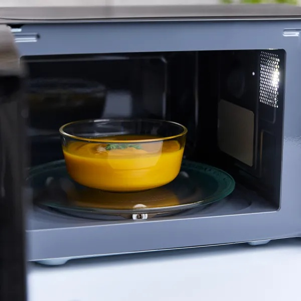 Widok wewnątrz kuchenki mikrofalowej. Miska z pomarańczową zupą na szklanym talerzu.